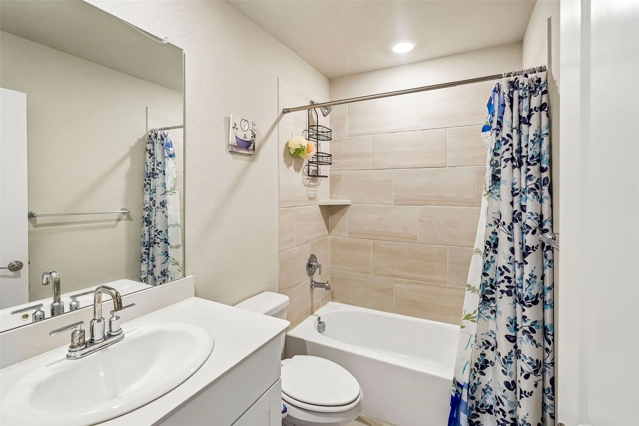 Recessed lighting, integrated bathtub, tiled shower surround, large vanity mirror, and polished chrome fixtures