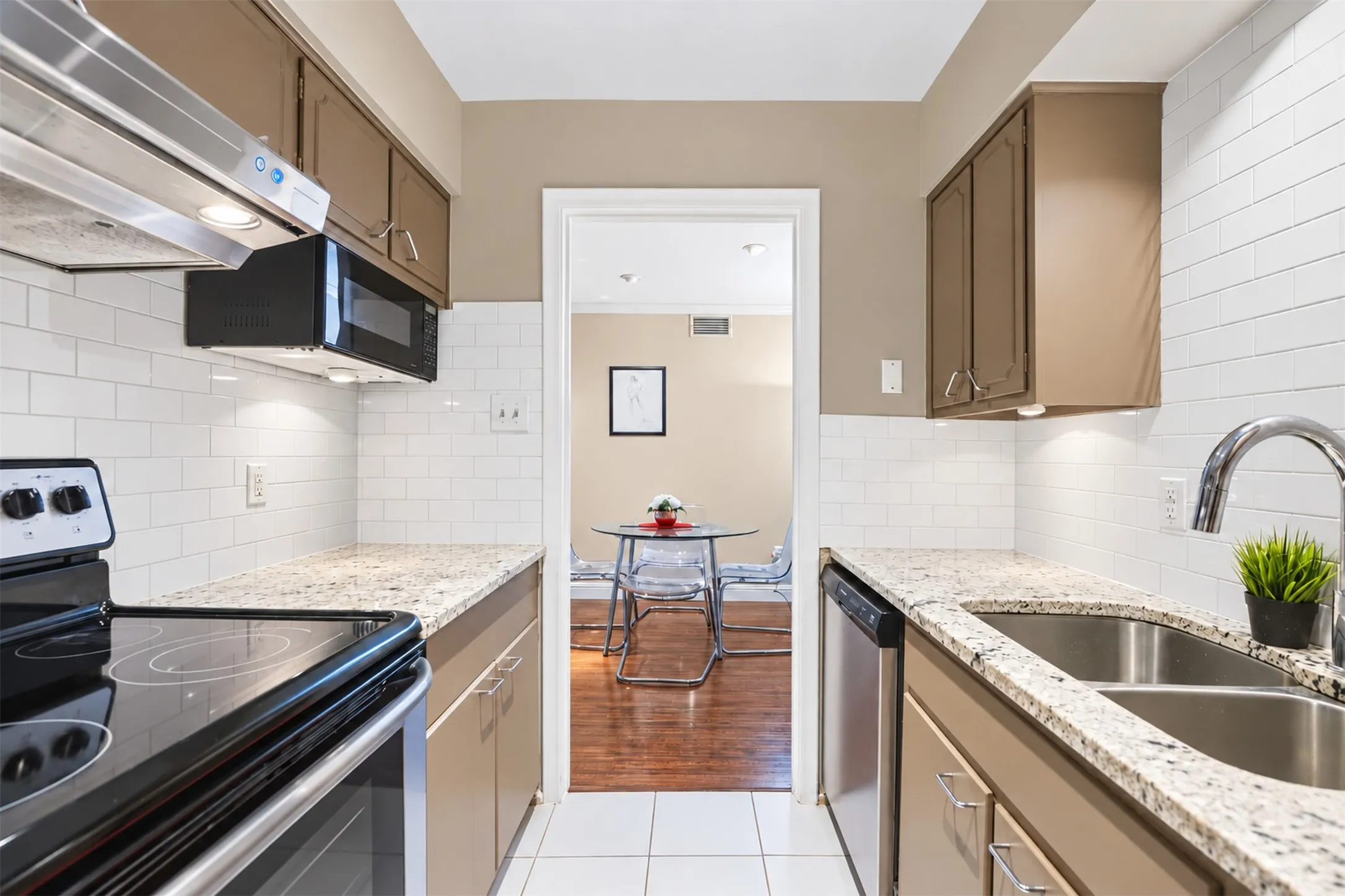 Galley kitchen featuring granite countertops, a white subway tile backsplash, stainless steel appliances, and under-cabinet lighting