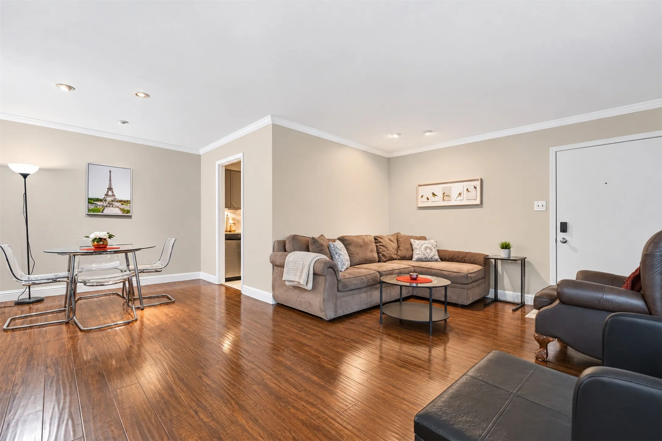Recessed lighting illuminates the open-concept living space, featuring wood-finish flooring and crown molding