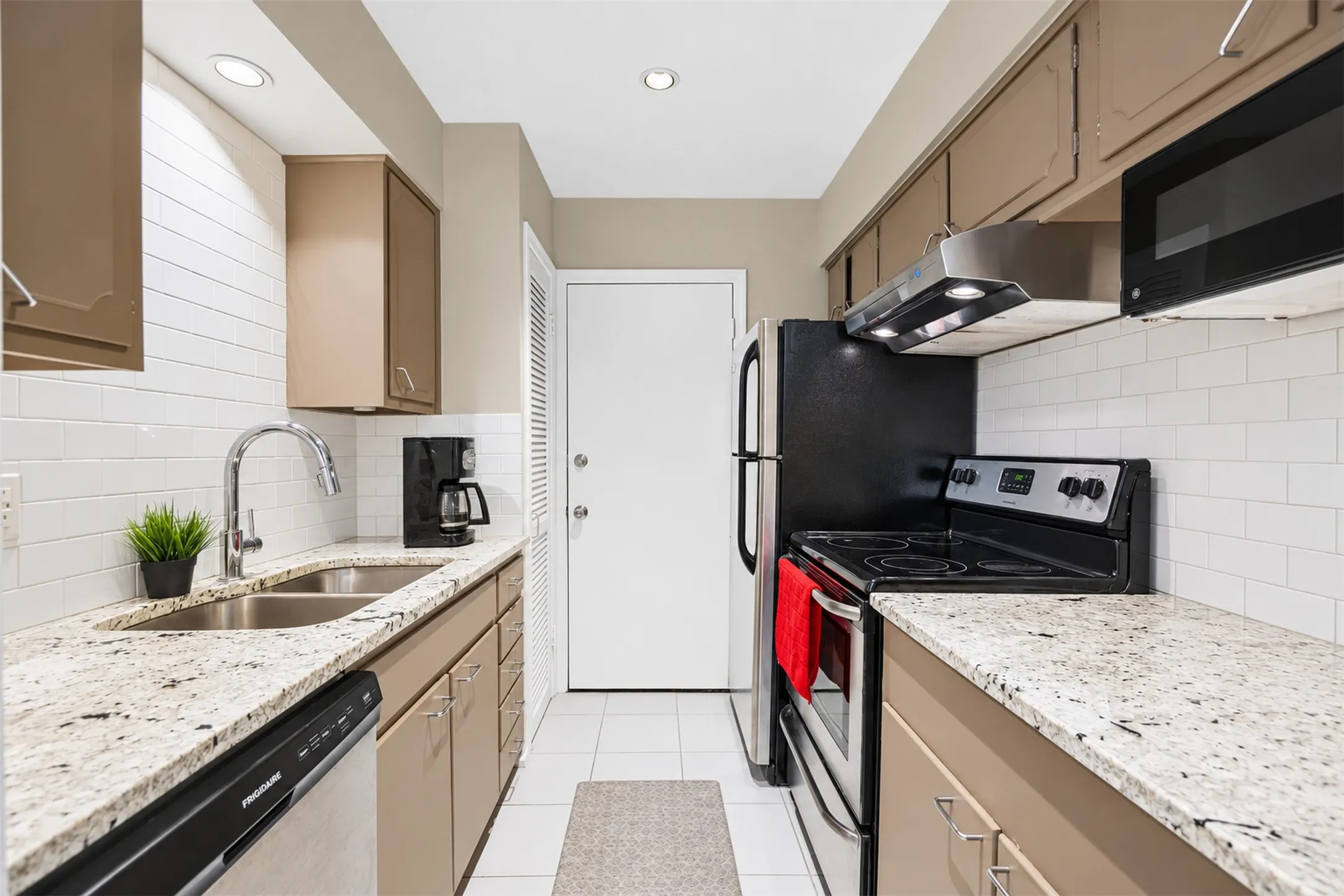 Kitchen featuring granite-style countertops, subway tile backsplash, recessed lighting, and stainless-steel appliances including a built-in microwave and range hood