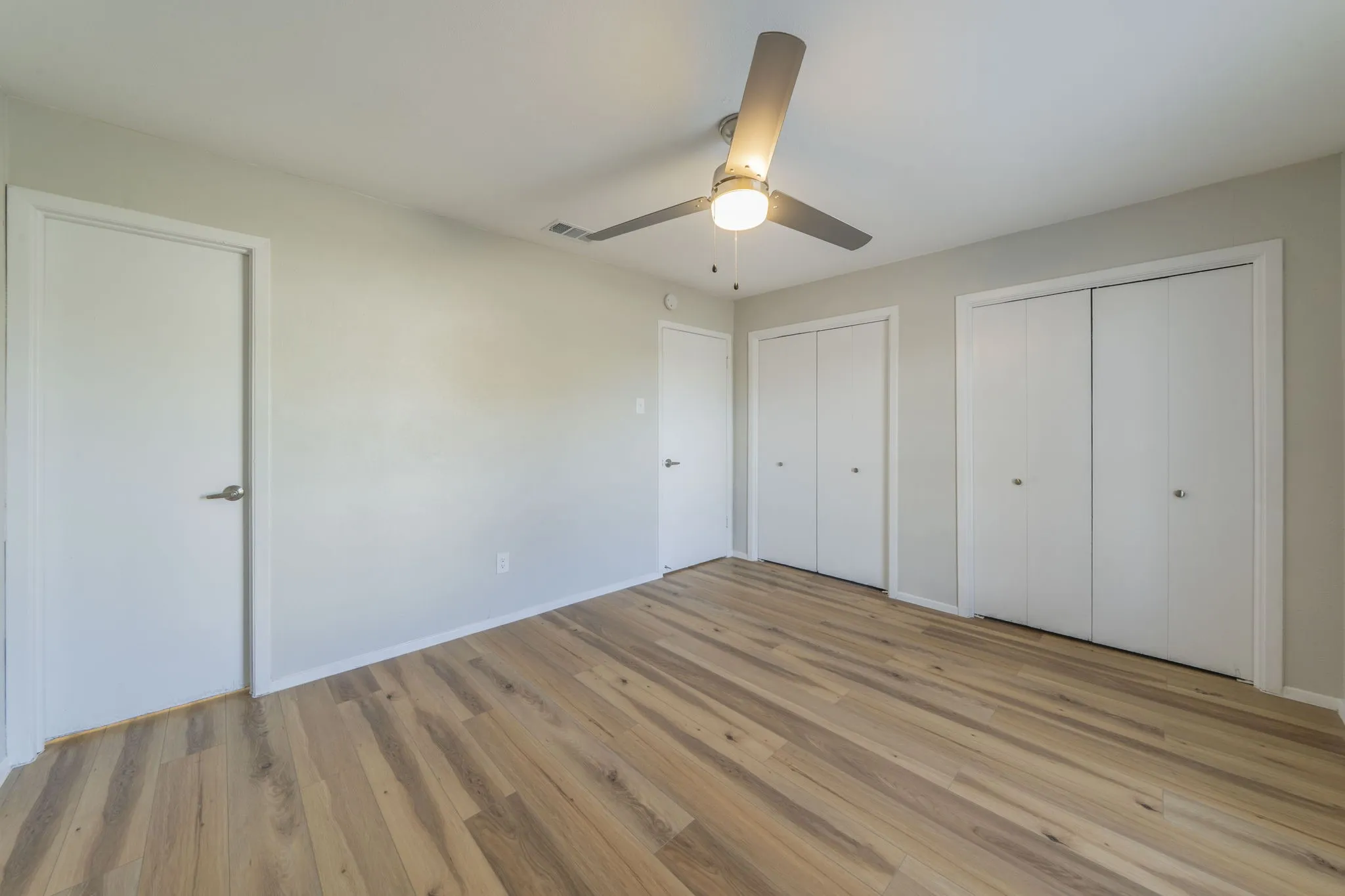 Light wood-finish flooring, neutral wall tones, modern ceiling fan with integrated lighting, and multiple closet storage options