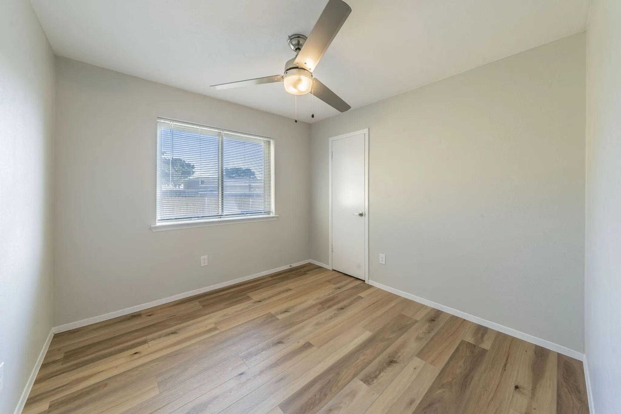 Wood-finish flooring, ceiling fan with integrated lighting, and a window with blinds