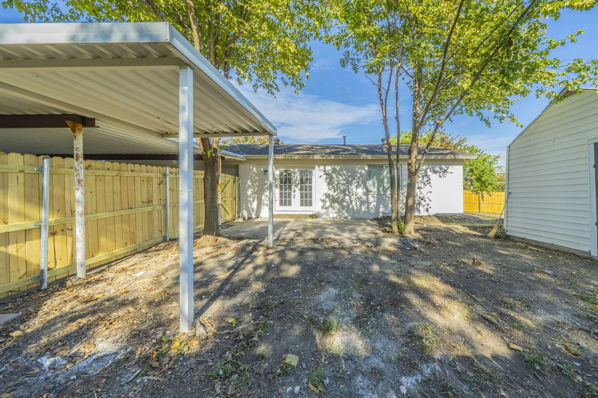 Covered carport structure, wood privacy fencing, white exterior siding, rear patio area, and exterior storage building