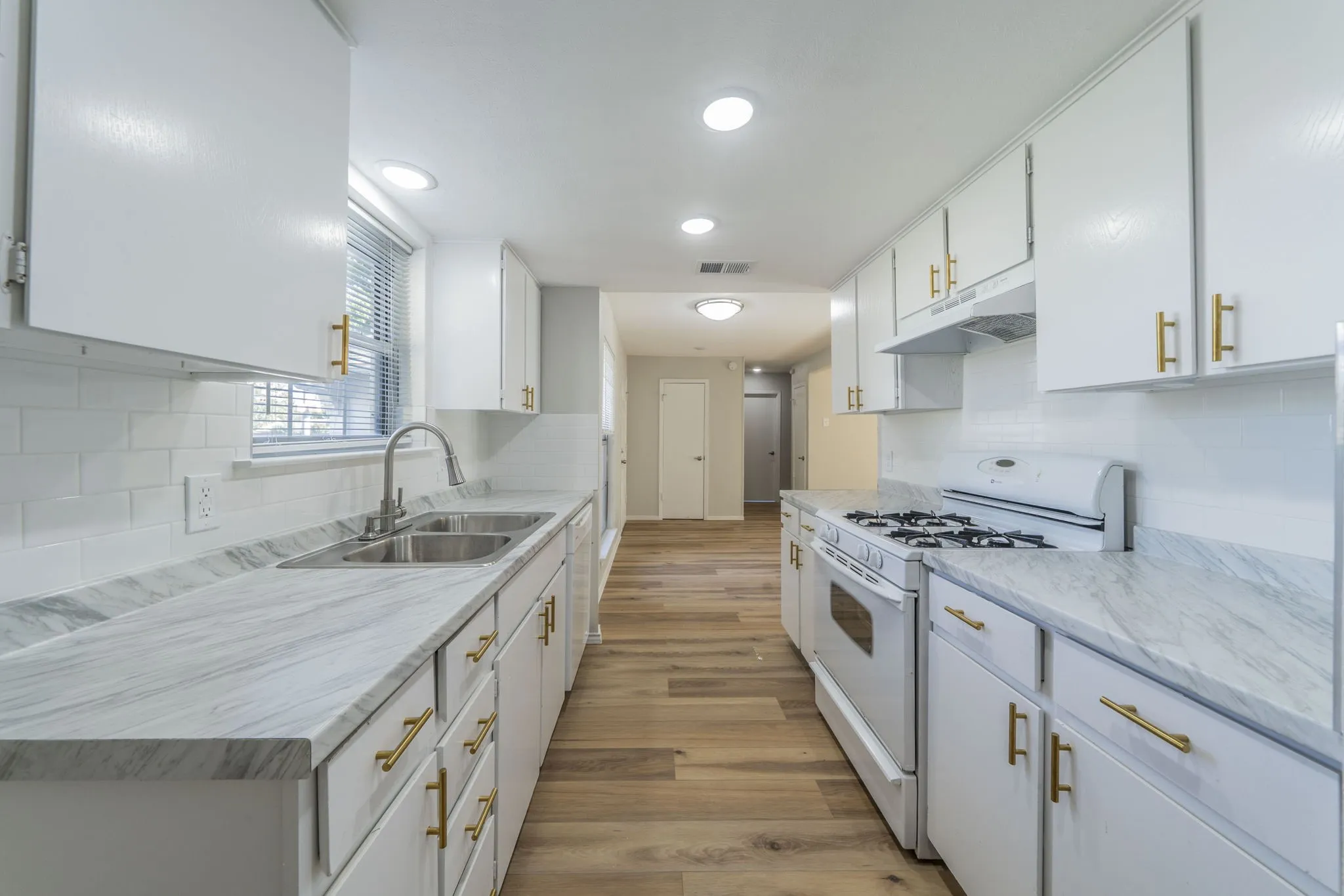 White cabinetry with gold-tone hardware, wood-finish flooring, white subway tile backsplash, and light-toned countertops