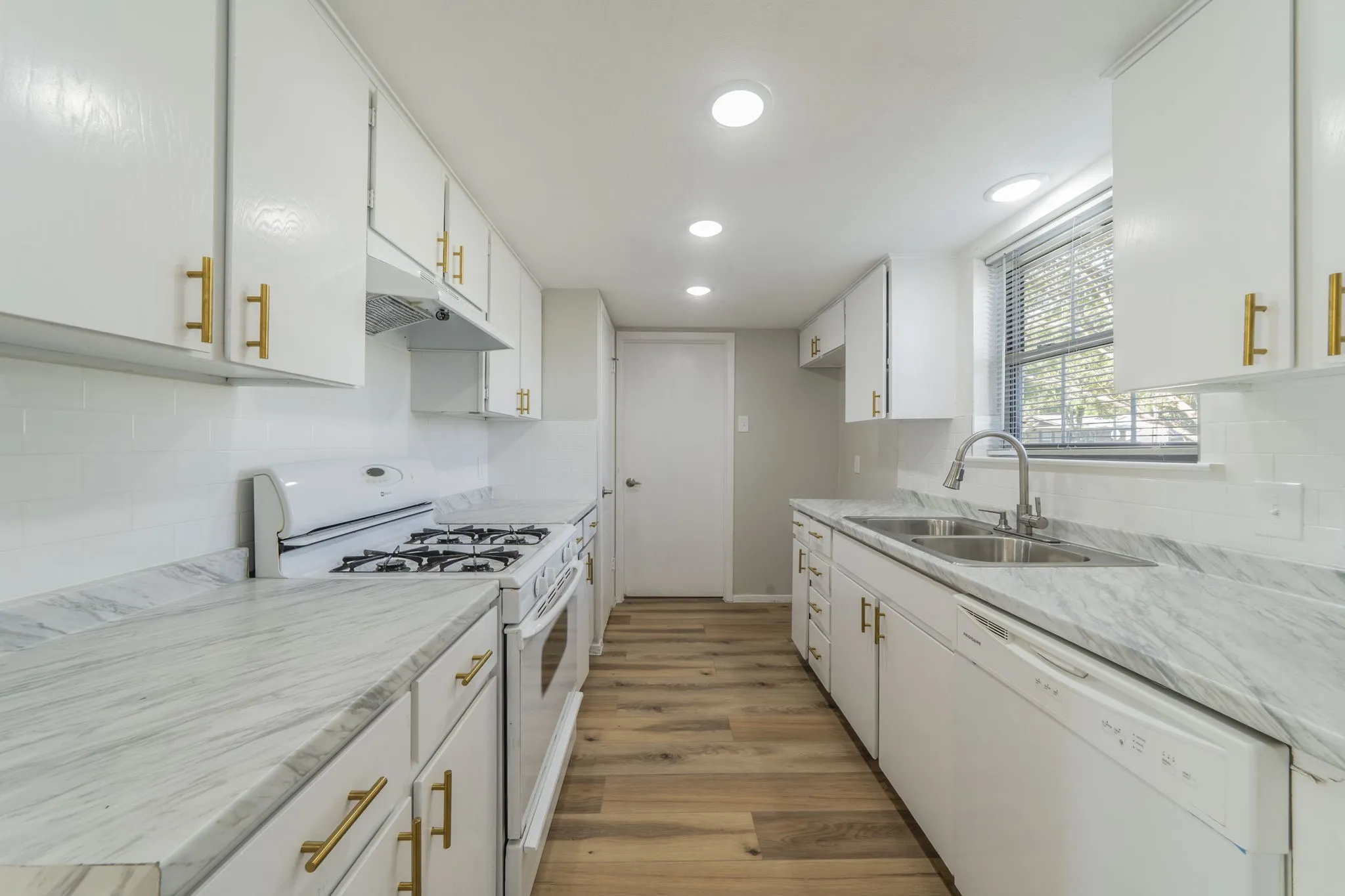 Kitchen featuring white cabinetry with gold-toned hardware, stone-look countertops, white subway tile backsplash, and wood-finish flooring