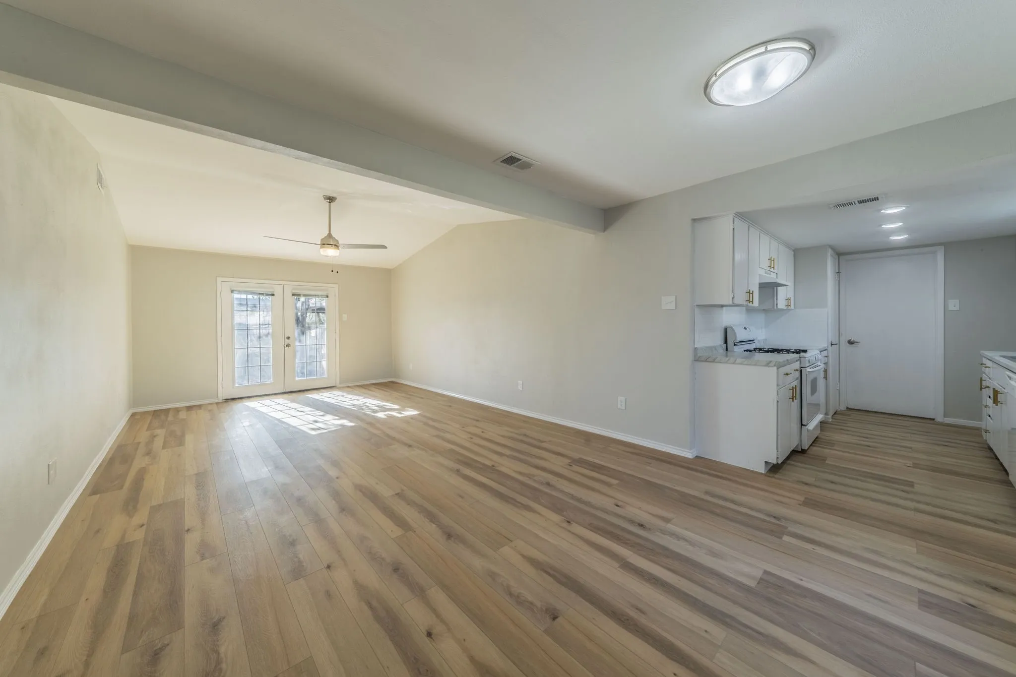 Vaulted ceiling, wood-finish flooring, ceiling fan, white kitchen cabinetry, and granite countertops