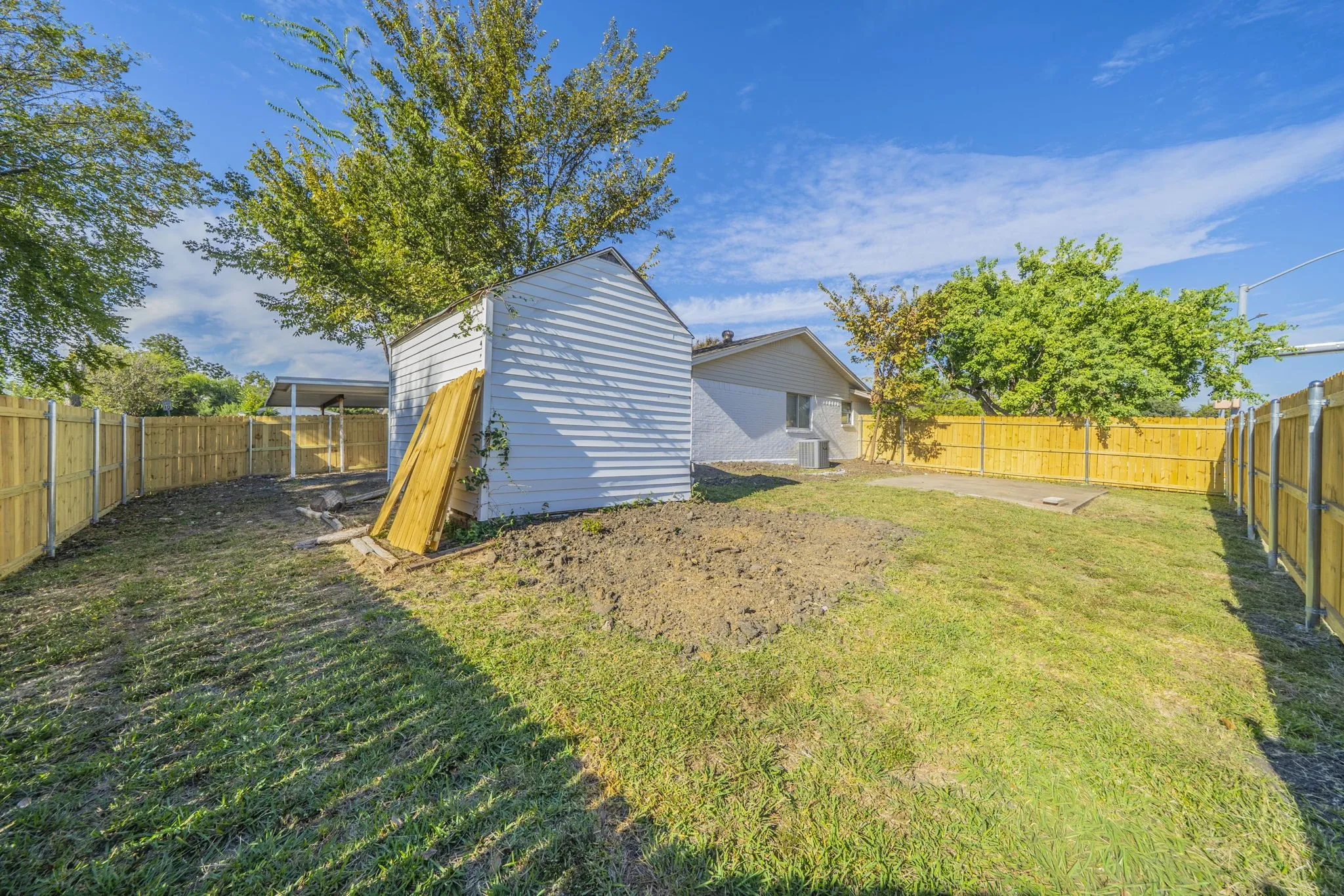 Expansive fenced backyard with a detached storage shed, lush green lawn, and mature trees