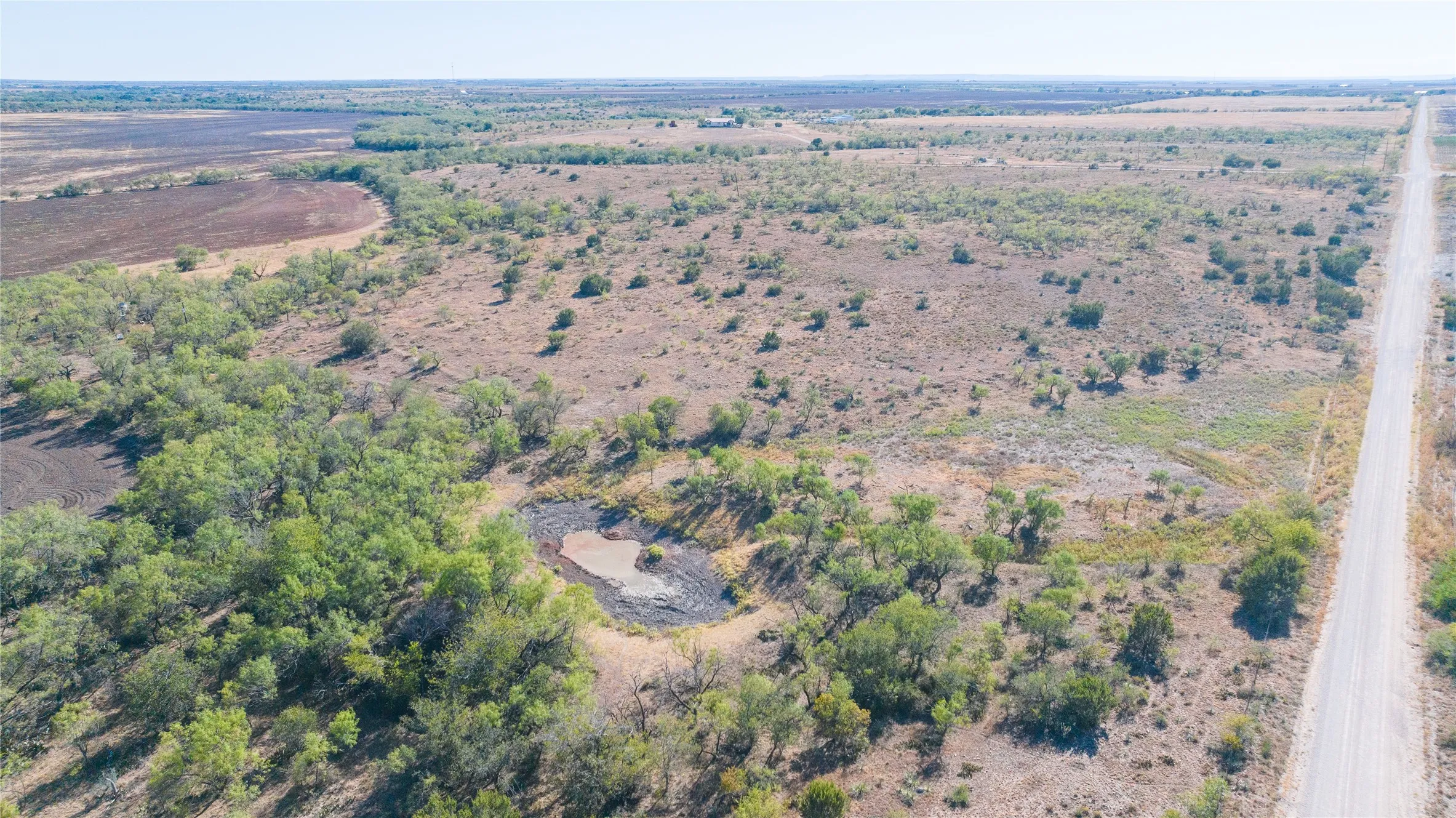 Expansive open terrain with natural vegetation, a dirt road, and a water feature
