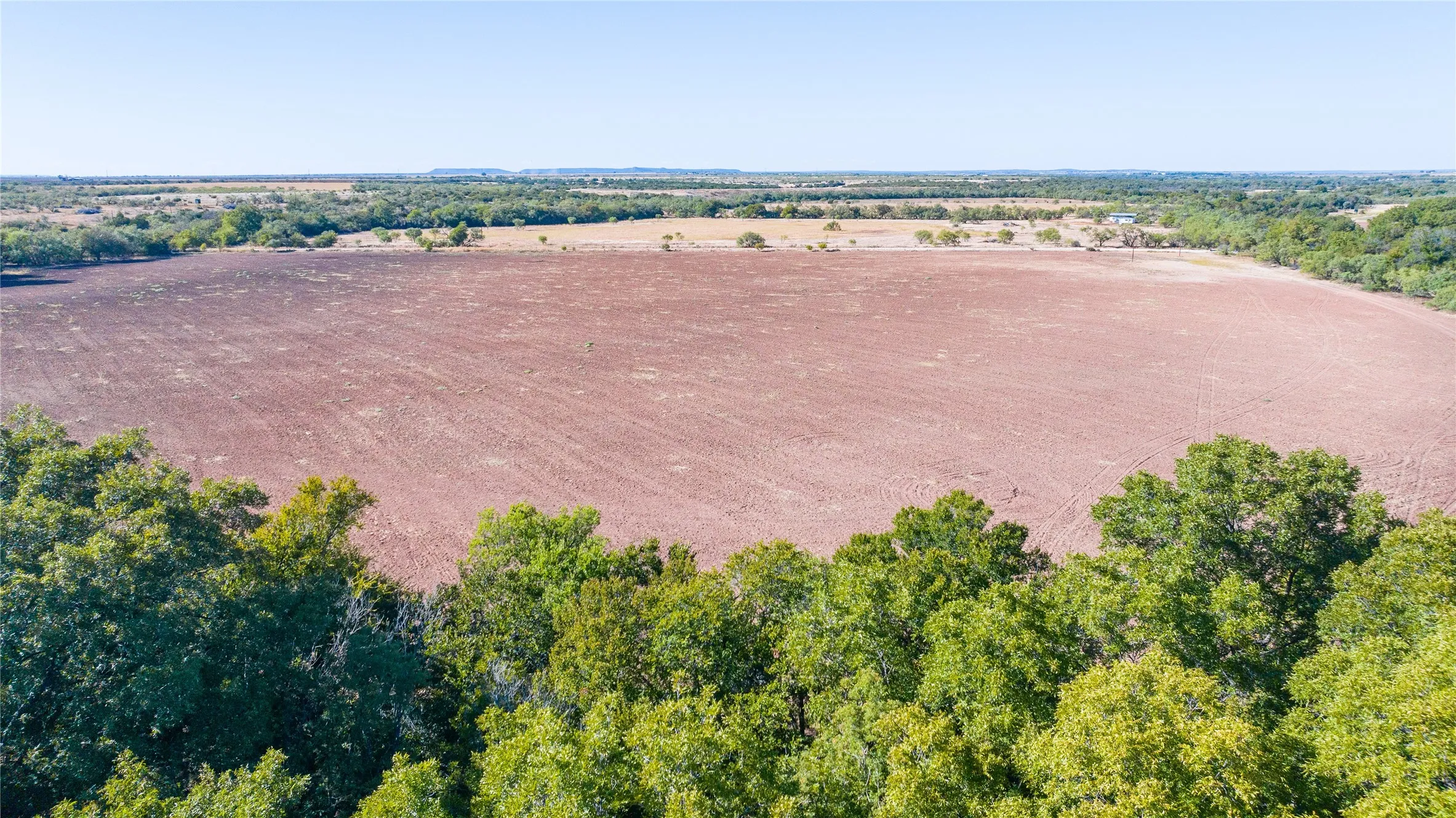 Expansive land parcel with cultivated earth, surrounded by mature trees