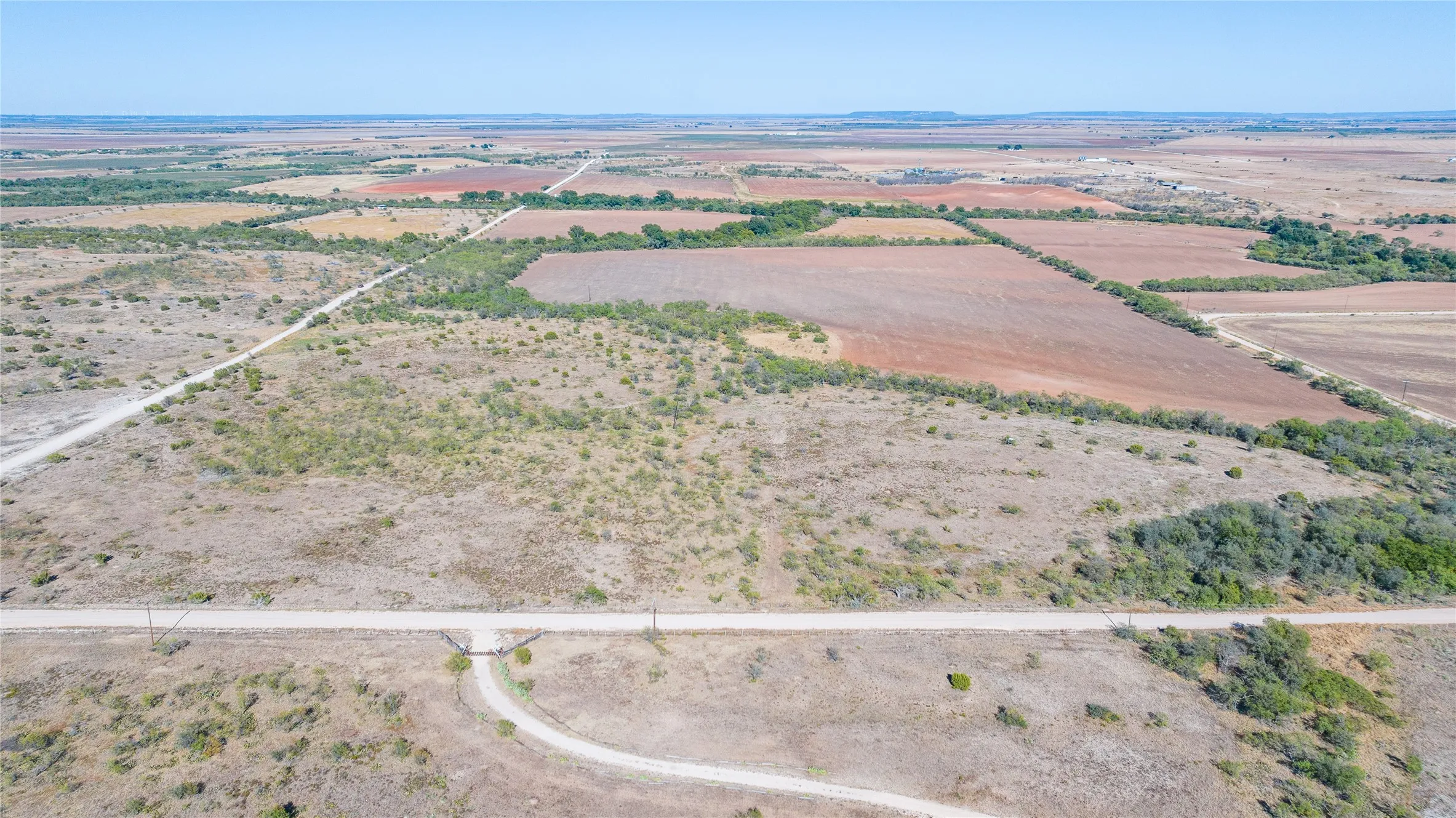 Expansive rural acreage featuring varied terrain, sections of cultivated land, natural vegetation, and a clear sky backdrop