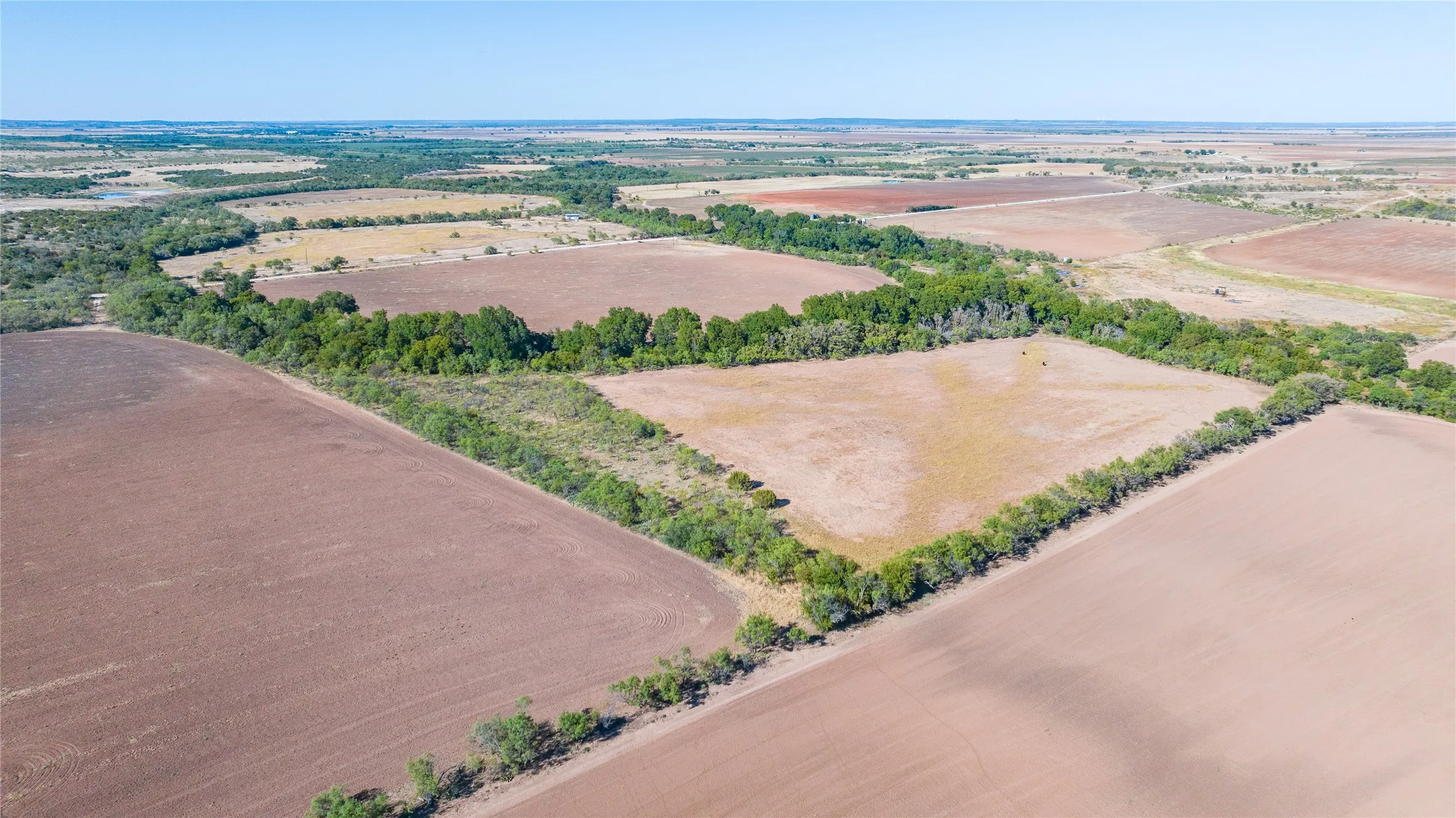 Expansive agricultural land featuring cultivated fields, natural tree lines, and open terrain