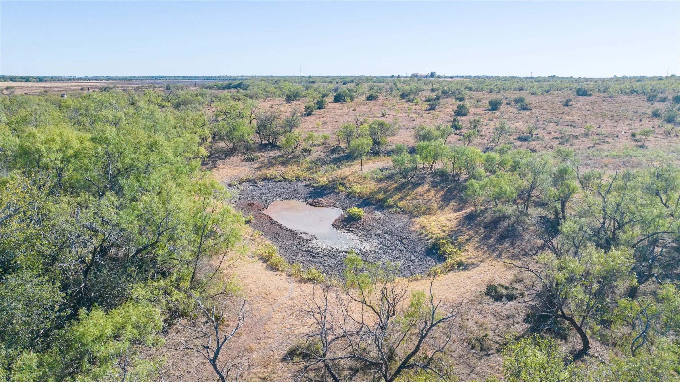 Expansive natural terrain featuring a small water body, scattered trees, and open land