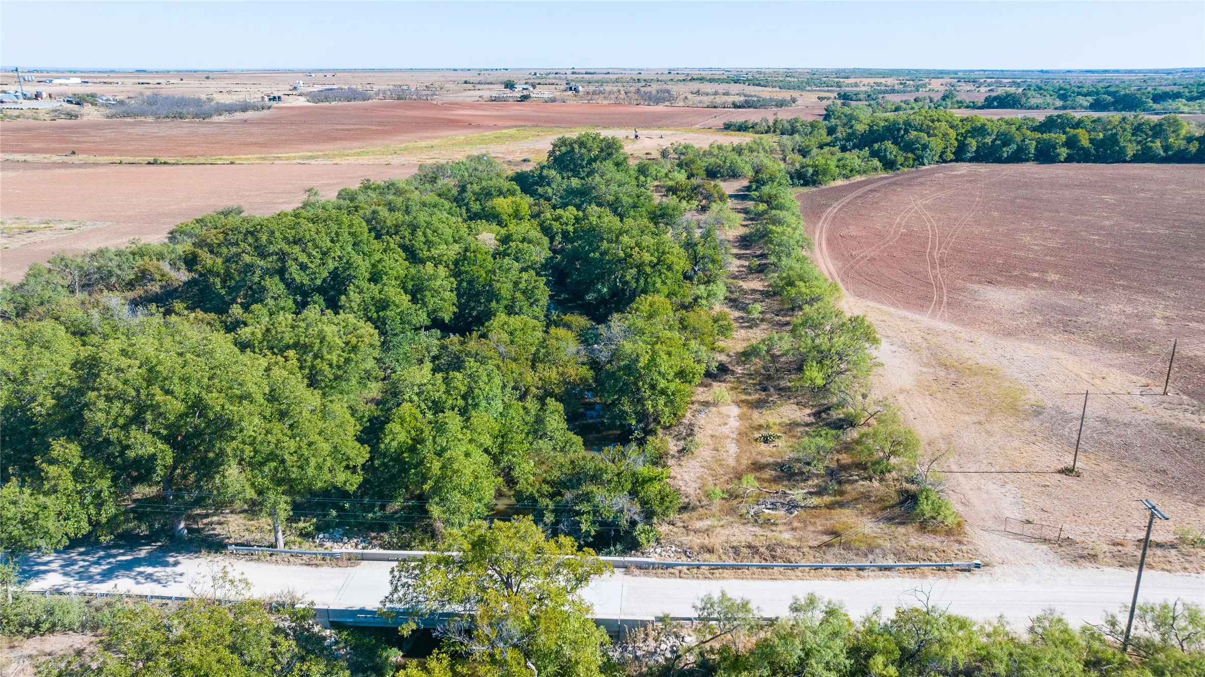 Expansive land featuring mature trees, open fields, and a paved road