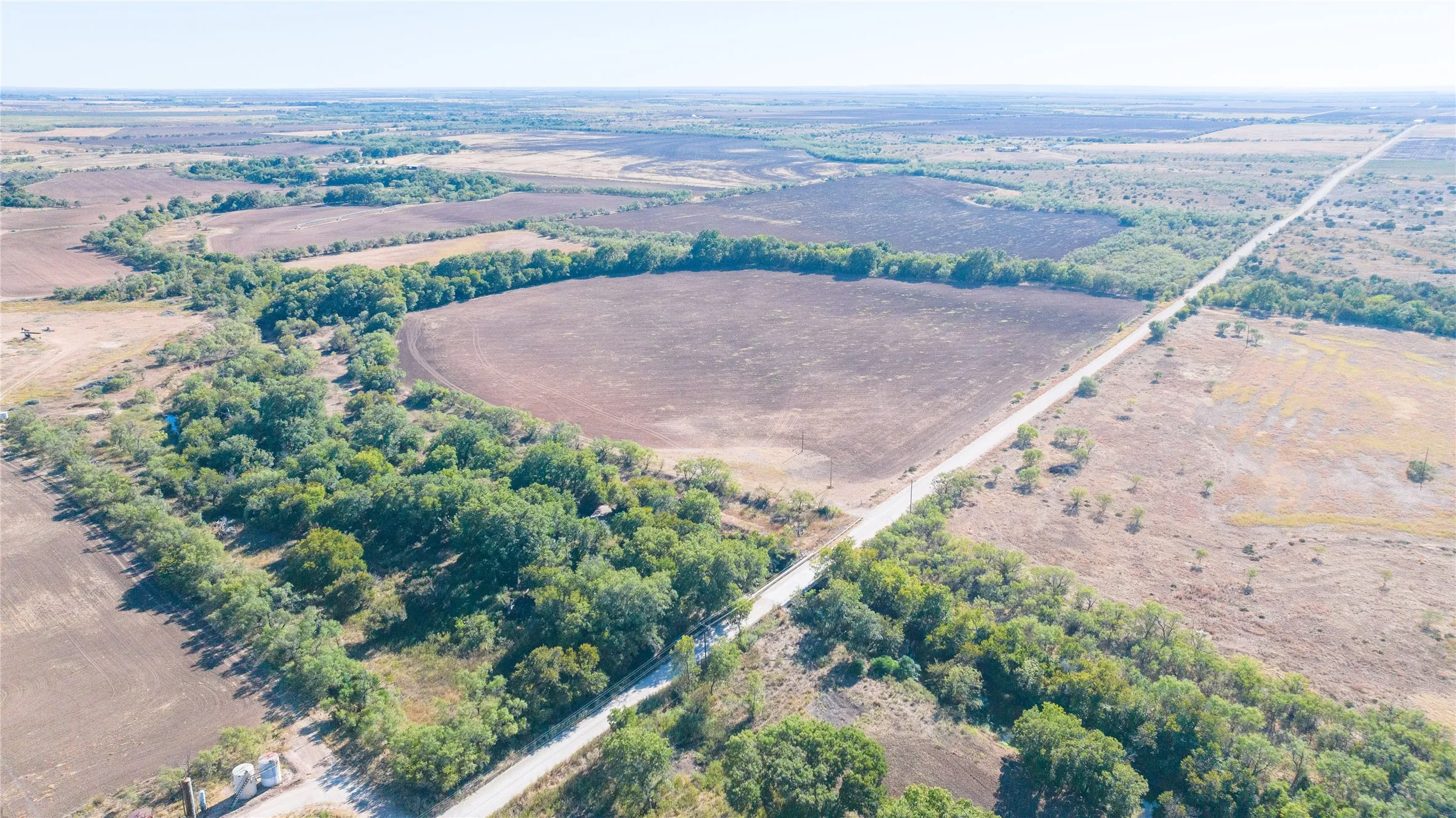 Expansive land offering a mix of open fields, wooded areas, and a paved road