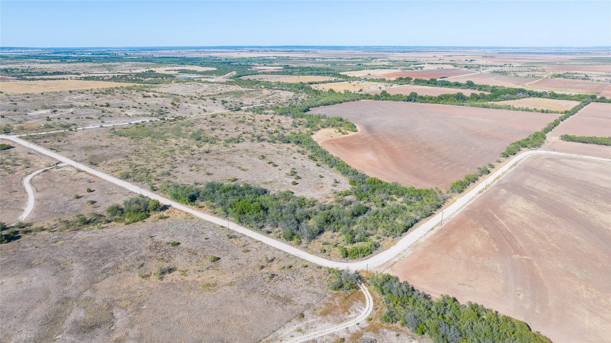Expansive open land with varied terrain, featuring cultivated fields and natural brush