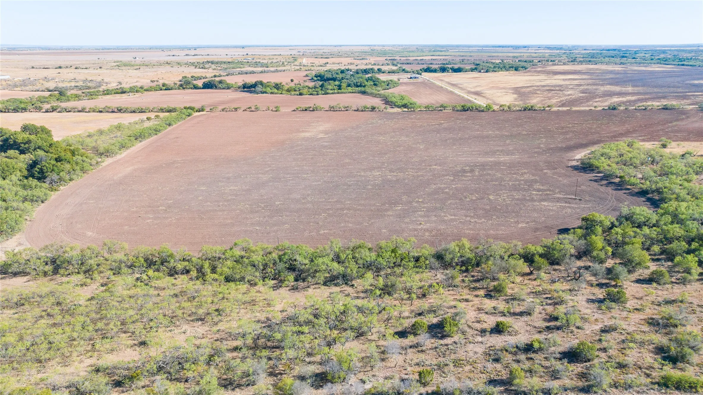 Expansive agricultural land featuring cultivated fields and natural tree lines