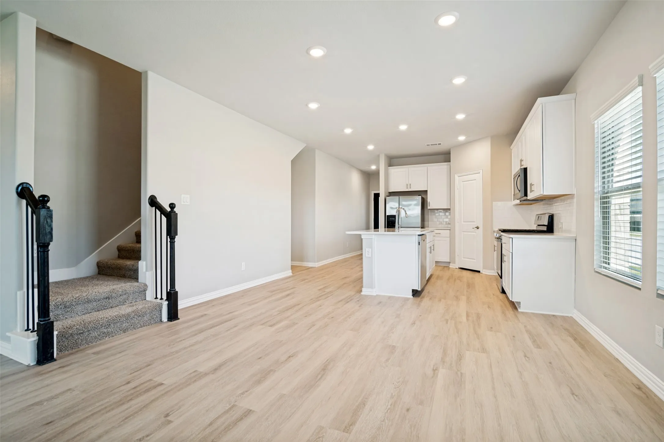 Open-concept living area featuring wood-finish flooring, recessed lighting, and a kitchen with white cabinetry