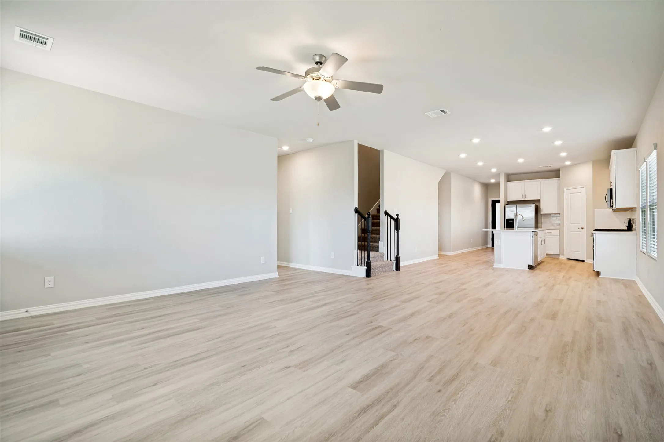 Open-concept living area with light wood-finish flooring, recessed lighting, and a ceiling fan