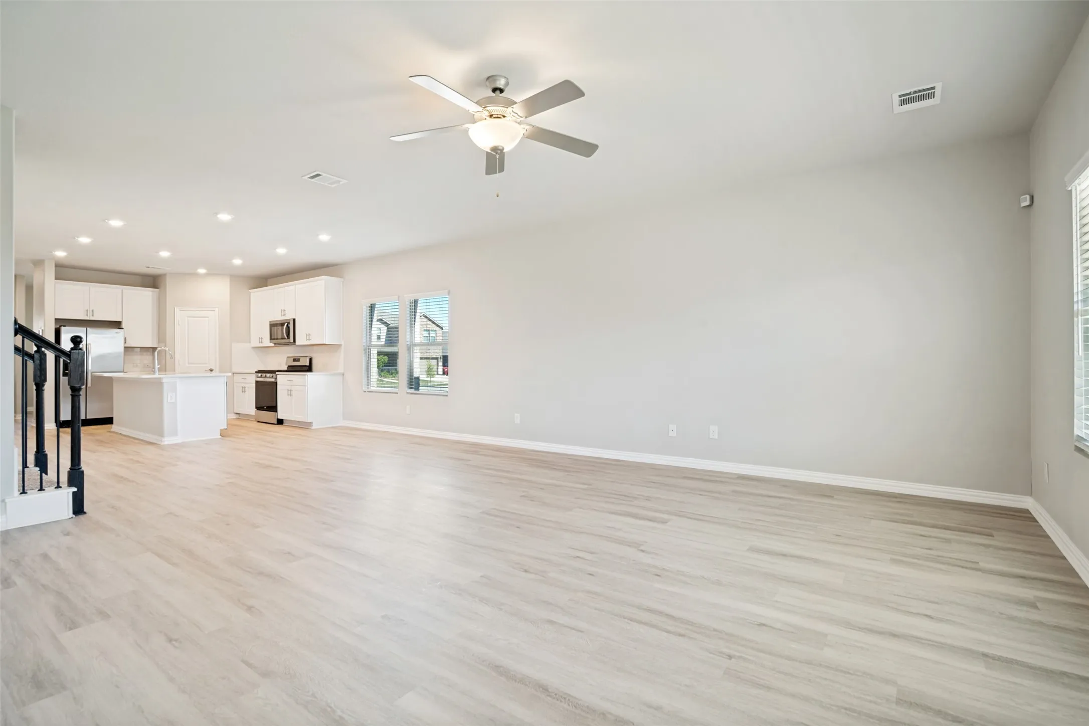 Light wood-finish flooring, white cabinetry, stainless steel appliances, recessed lighting, and a ceiling fan