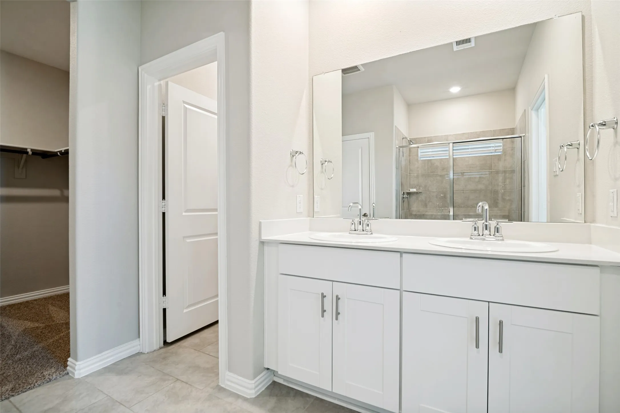 Dual vanity with white cabinetry and chrome fixtures, large rectangular mirror, and gray tile flooring