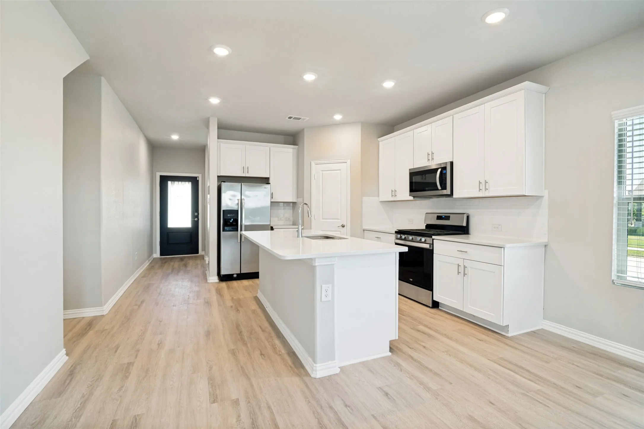 Open concept living area with wood-finish flooring, recessed lighting, and a kitchen featuring white cabinetry, a central island, and stainless steel appliances