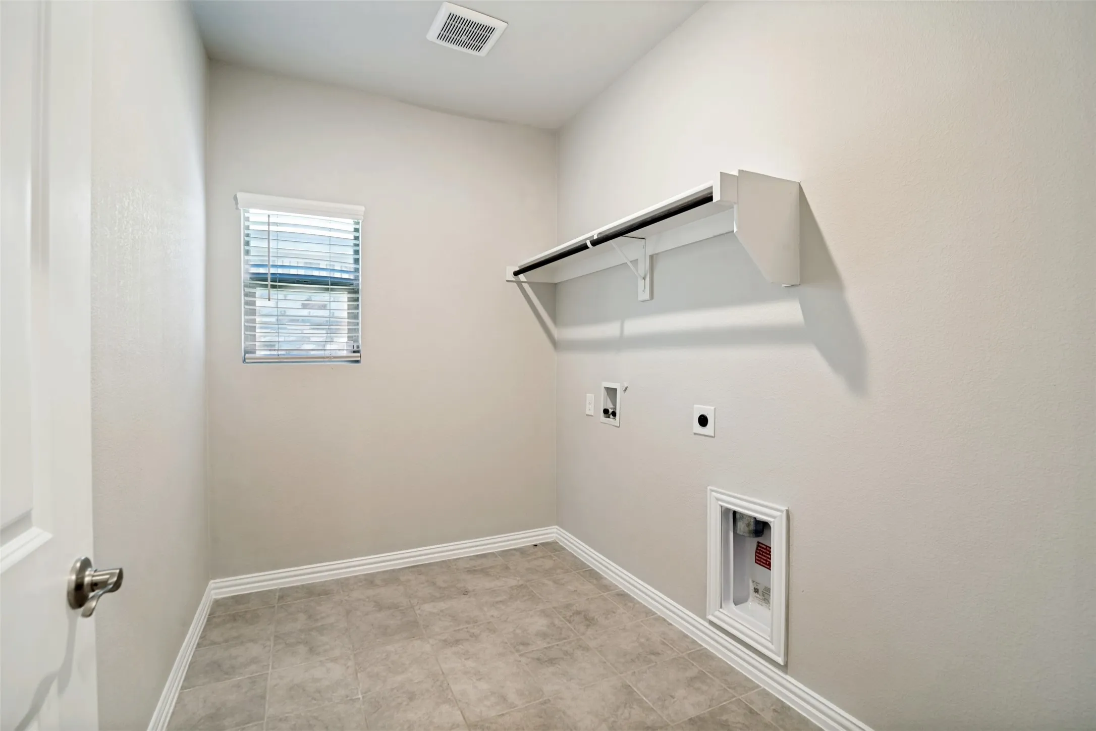 Built-in shelving with hanging rod, window with blinds, tile flooring, and utility hookups