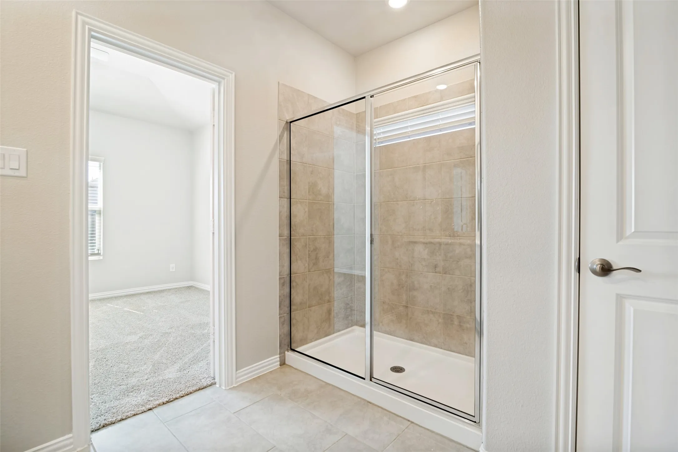 Glass-enclosed shower with tile surround, neutral wall paint, recessed lighting, and tile flooring