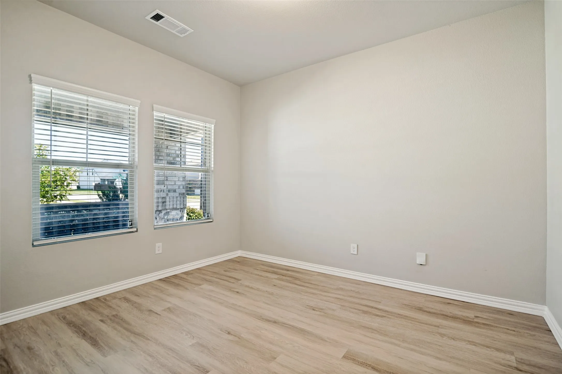 Recessed ceiling light, wood-finish flooring, two windows with blinds, and light-toned walls