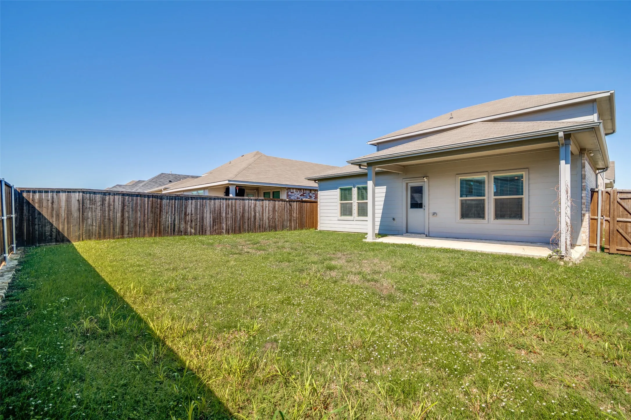 Expansive backyard with a covered patio, wood privacy fencing, and multiple exterior windows