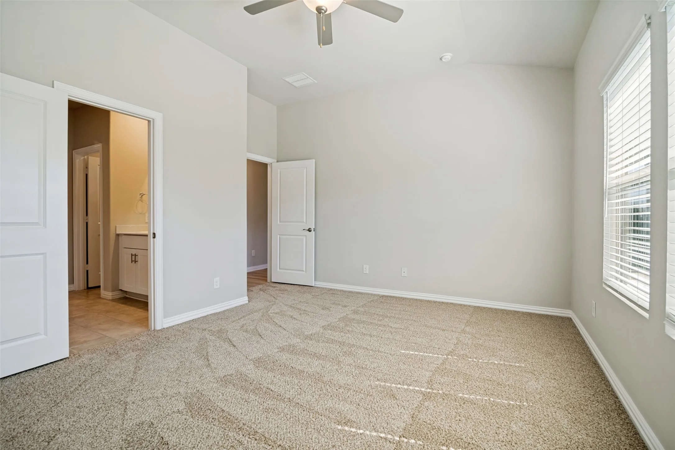Vaulted ceiling with a ceiling fan, light-colored carpet, multiple windows with blinds, and white interior doors