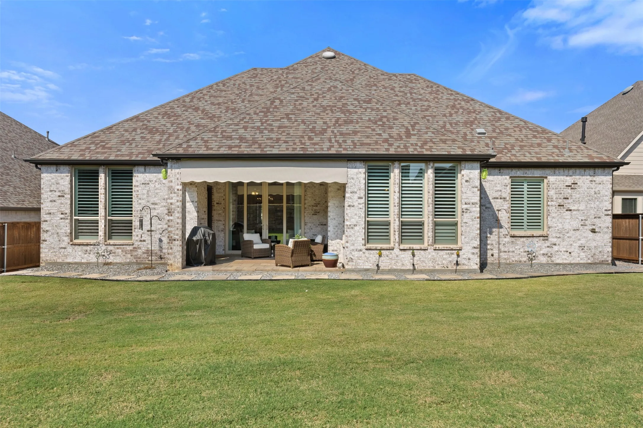 Expansive backyard with a covered patio, featuring a retractable awning, stone paver patio, and a manicured lawn
