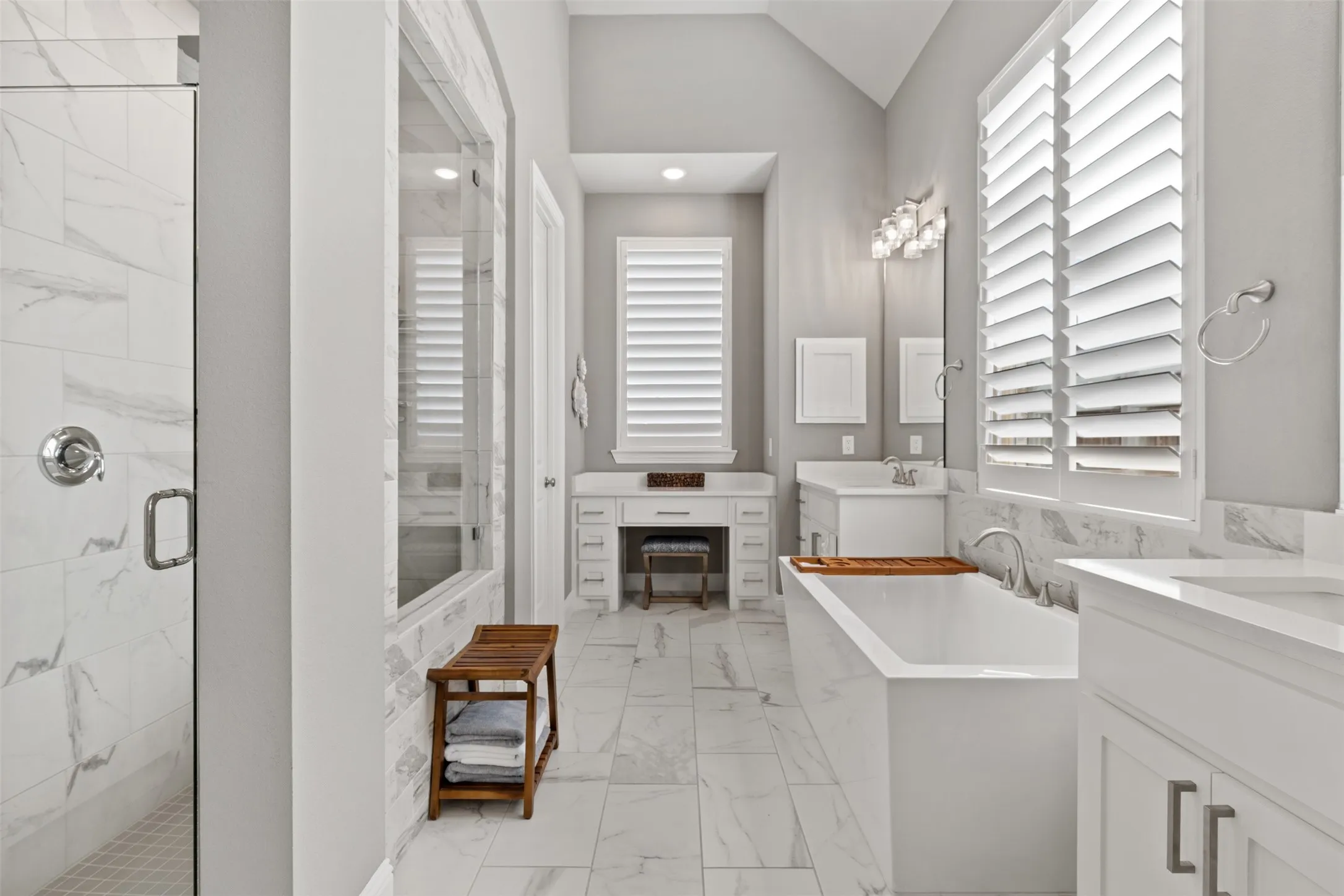Primary bathroom featuring walk-in shower with clear glass enclosure, freestanding soaking tub, dual vanity with and plantation shutters