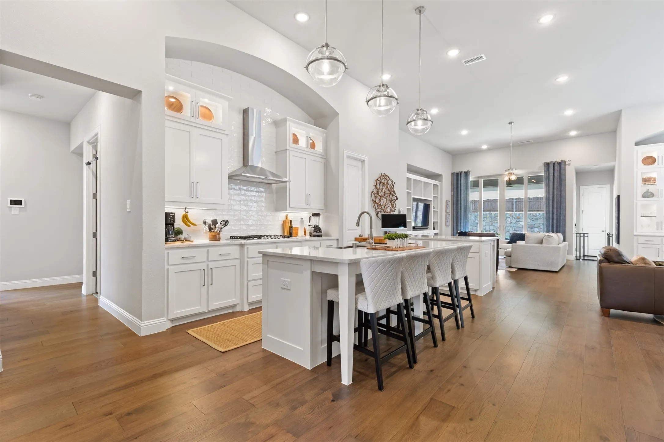 Open-concept living space featuring wood-finish flooring, a white kitchen island with counter seating, pendant lighting, recessed lighting, and white cabinetry