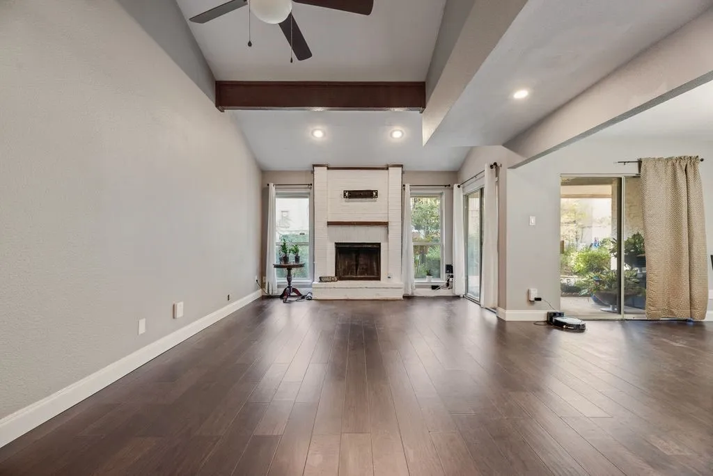 Vaulted ceiling with exposed beam, dark wood-finish flooring, recessed lighting, white brick fireplace, and sliding glass doors