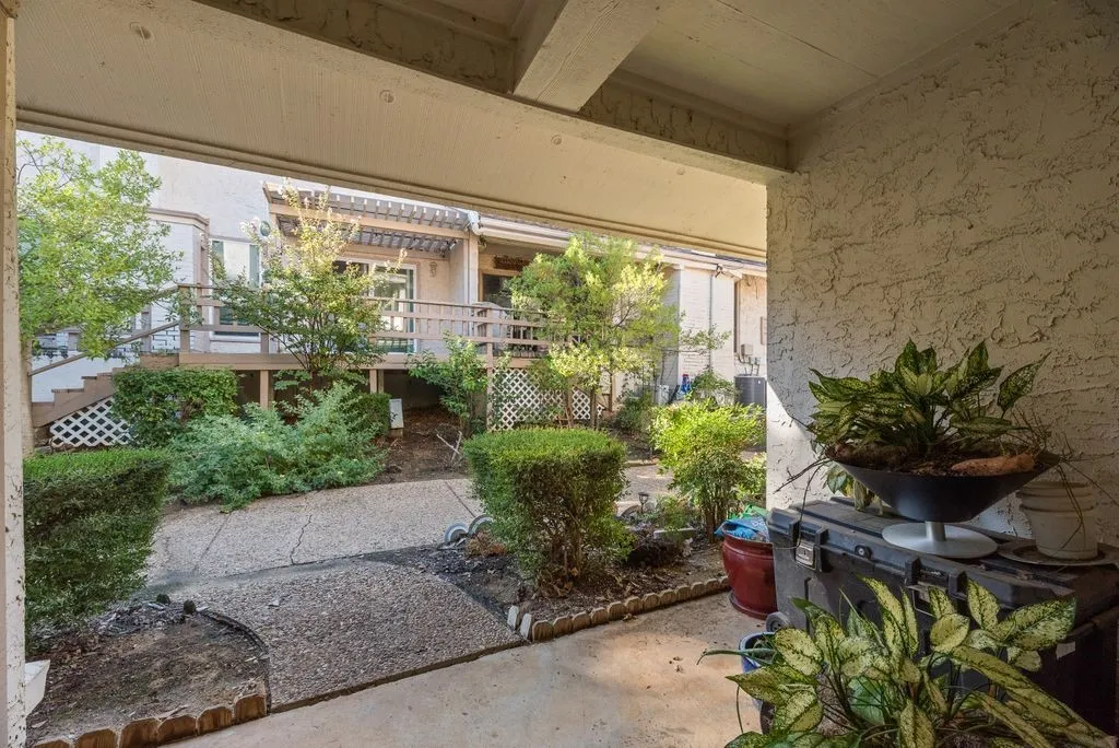 Exterior stucco finish, covered patio, concrete pathway, decorative lattice accents, and mature landscaping