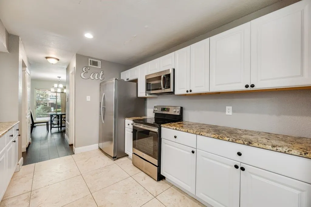 Kitchen featuring white cabinetry, stone countertops, stainless steel appliances, and tile flooring