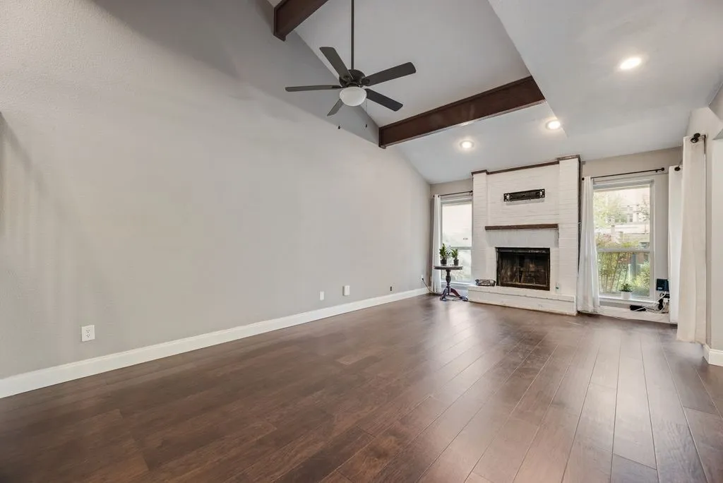 Vaulted ceiling with exposed wood beams, ceiling fan, recessed lighting, wood-finish flooring, and a white brick fireplace