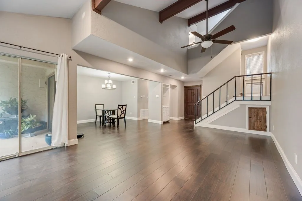 High ceilings with exposed wood beams, dark wood-finish flooring, a contemporary ceiling fan, and a prominent staircase with metal railings