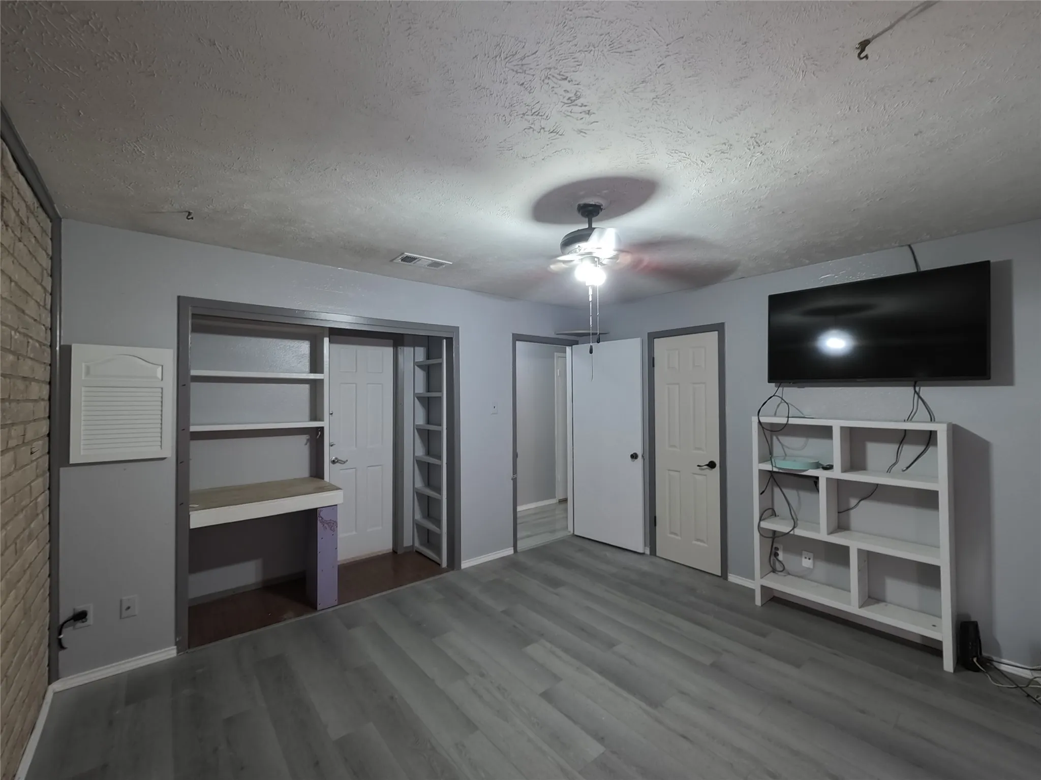 Wood-finish flooring, built-in shelving, ceiling fan, and painted brick accent wall