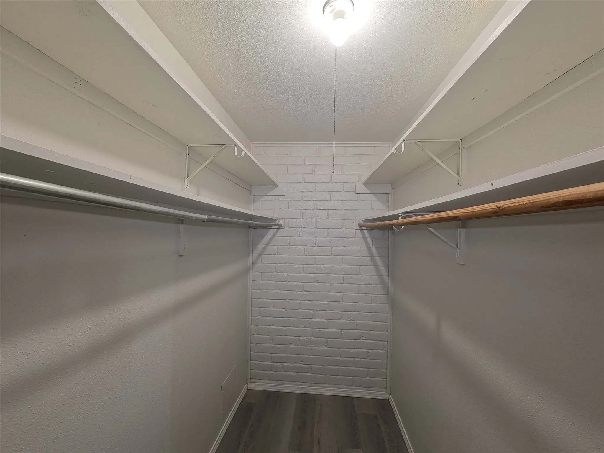 Walk-in closet with brick accent wall, wood-finish flooring, and dual hanging rods