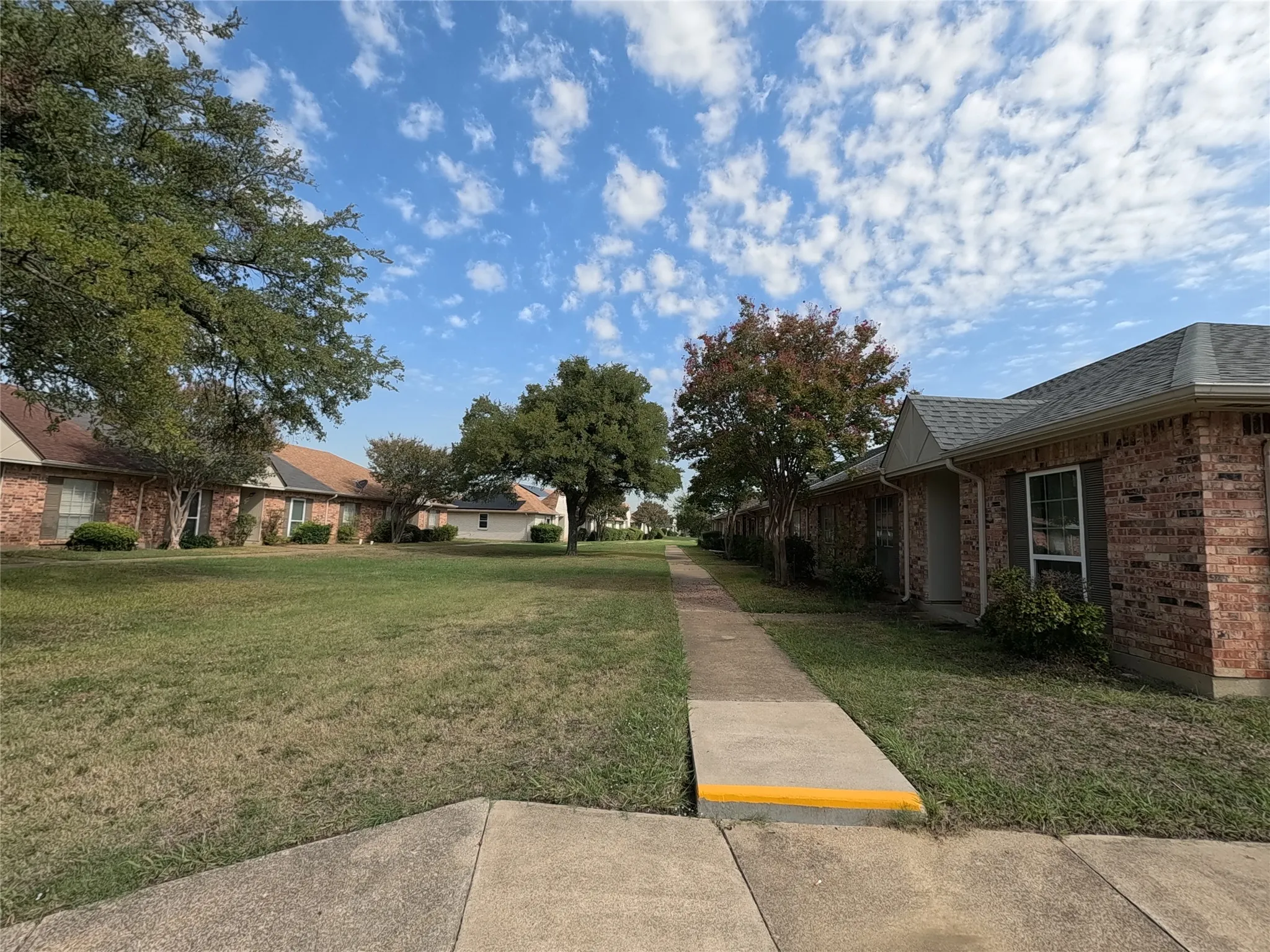 Brick exterior residence with a gabled roofline, mature trees, and a concrete walkway