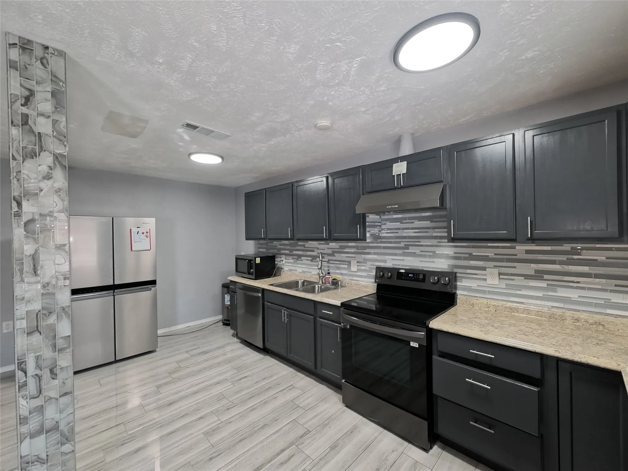 Kitchen featuring dark cabinetry, light-toned countertops, stainless steel appliances, a tile backsplash, and wood-finish flooring