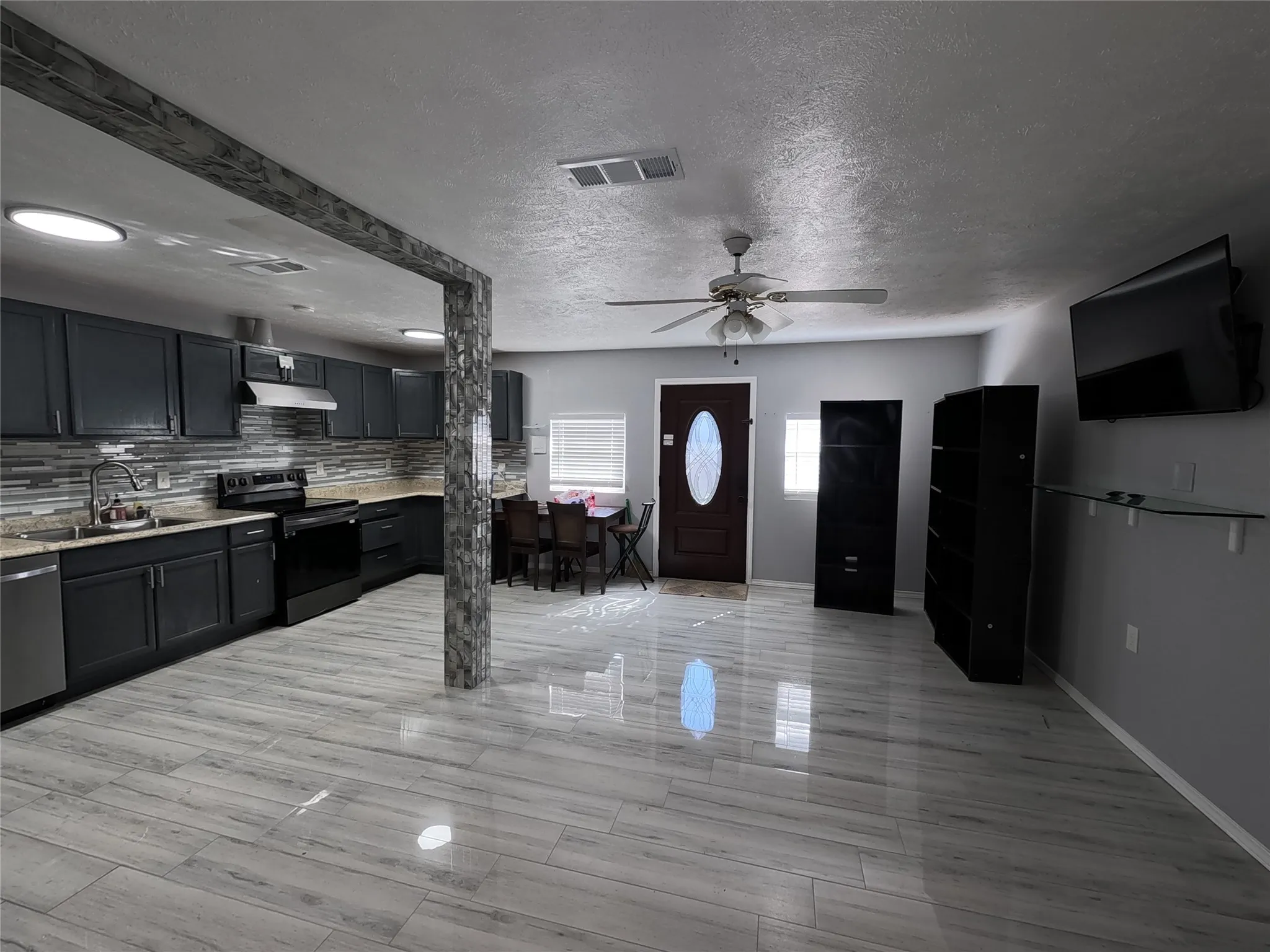 Open-concept living space with wood-finish flooring, a contemporary kitchen featuring dark cabinetry and a tiled backsplash, and recessed lighting