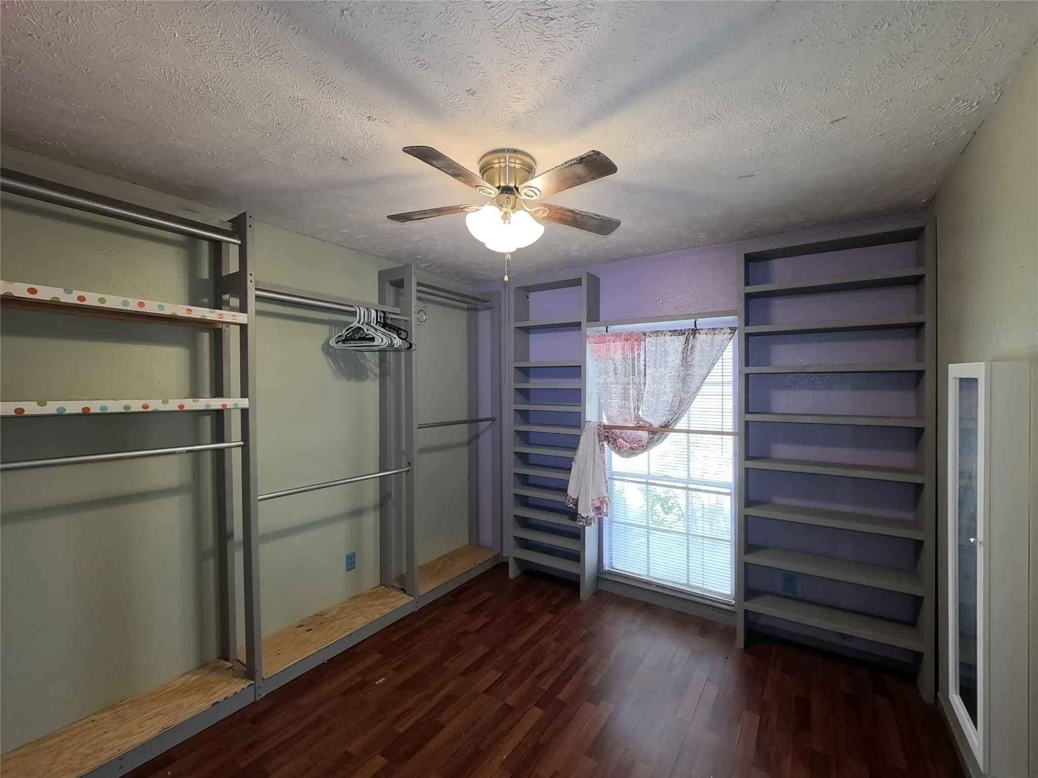 Wood-finish flooring, built-in shelving, built-in clothing rods, and ceiling fan with integrated lighting