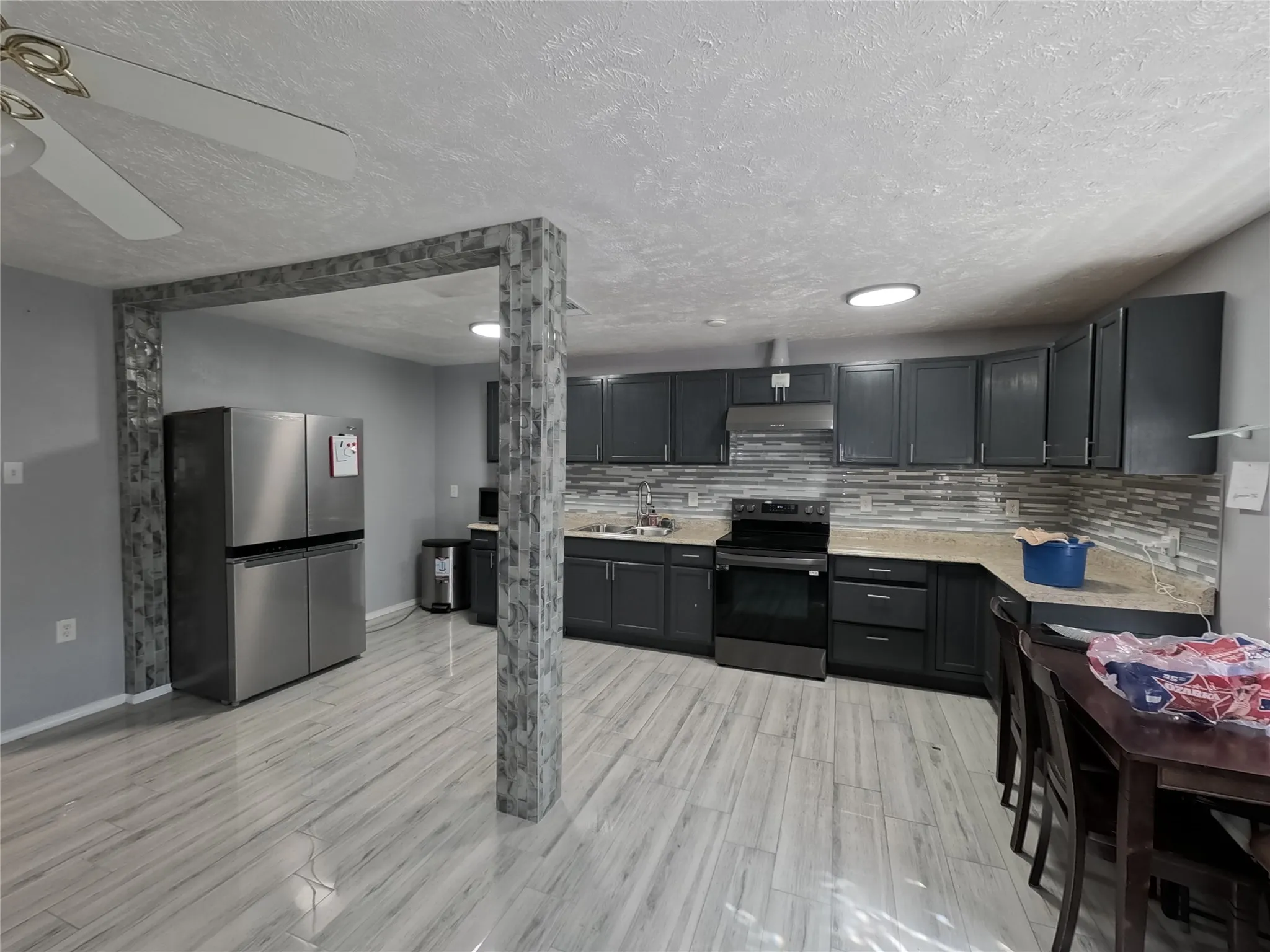 Kitchen with wood-finish flooring, dark cabinetry, light-toned countertops, and a tiled backsplash