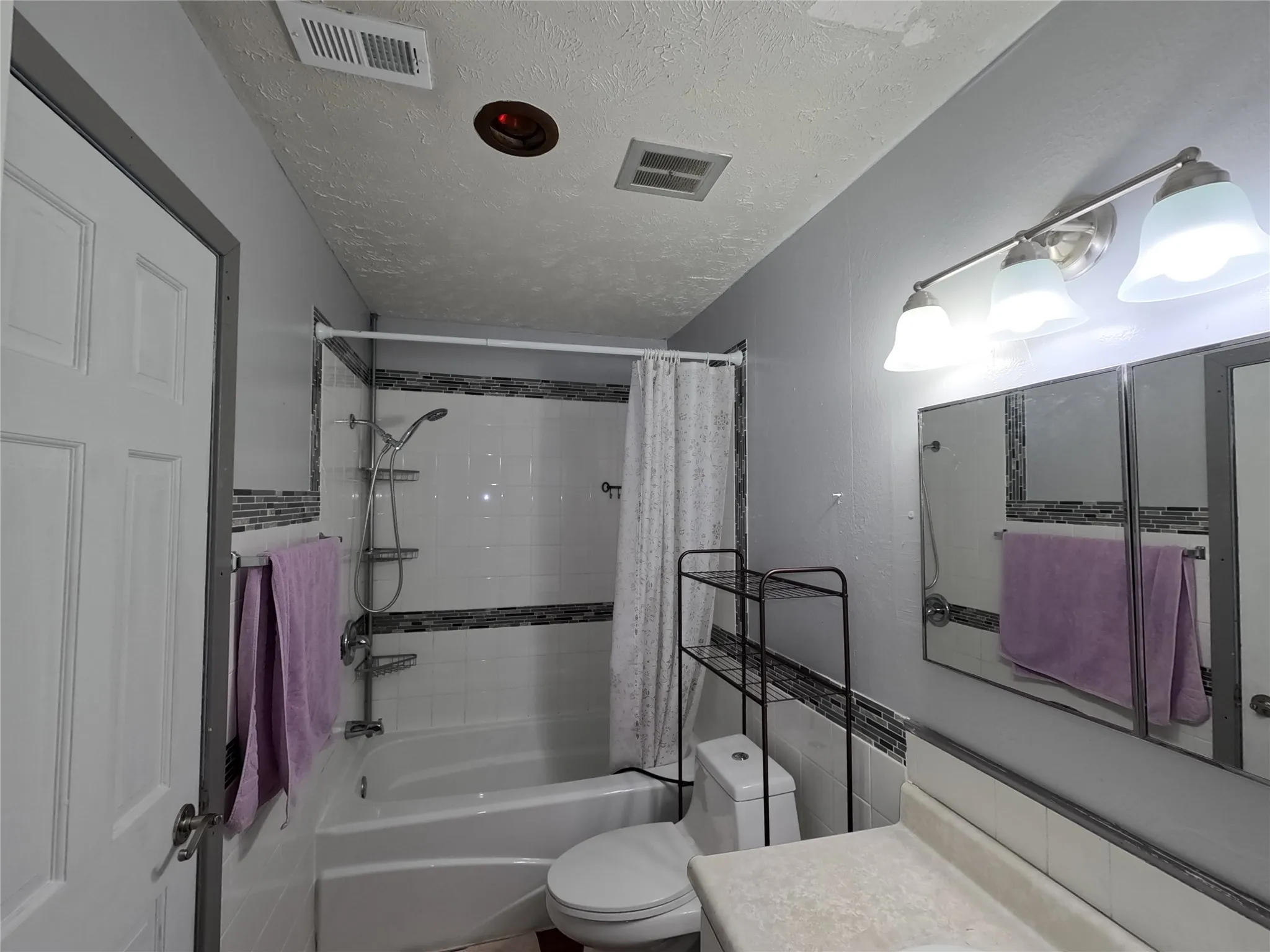 Bathroom featuring a white bathtub, white tile surround with decorative accent band, and a vanity with a light-colored countertop