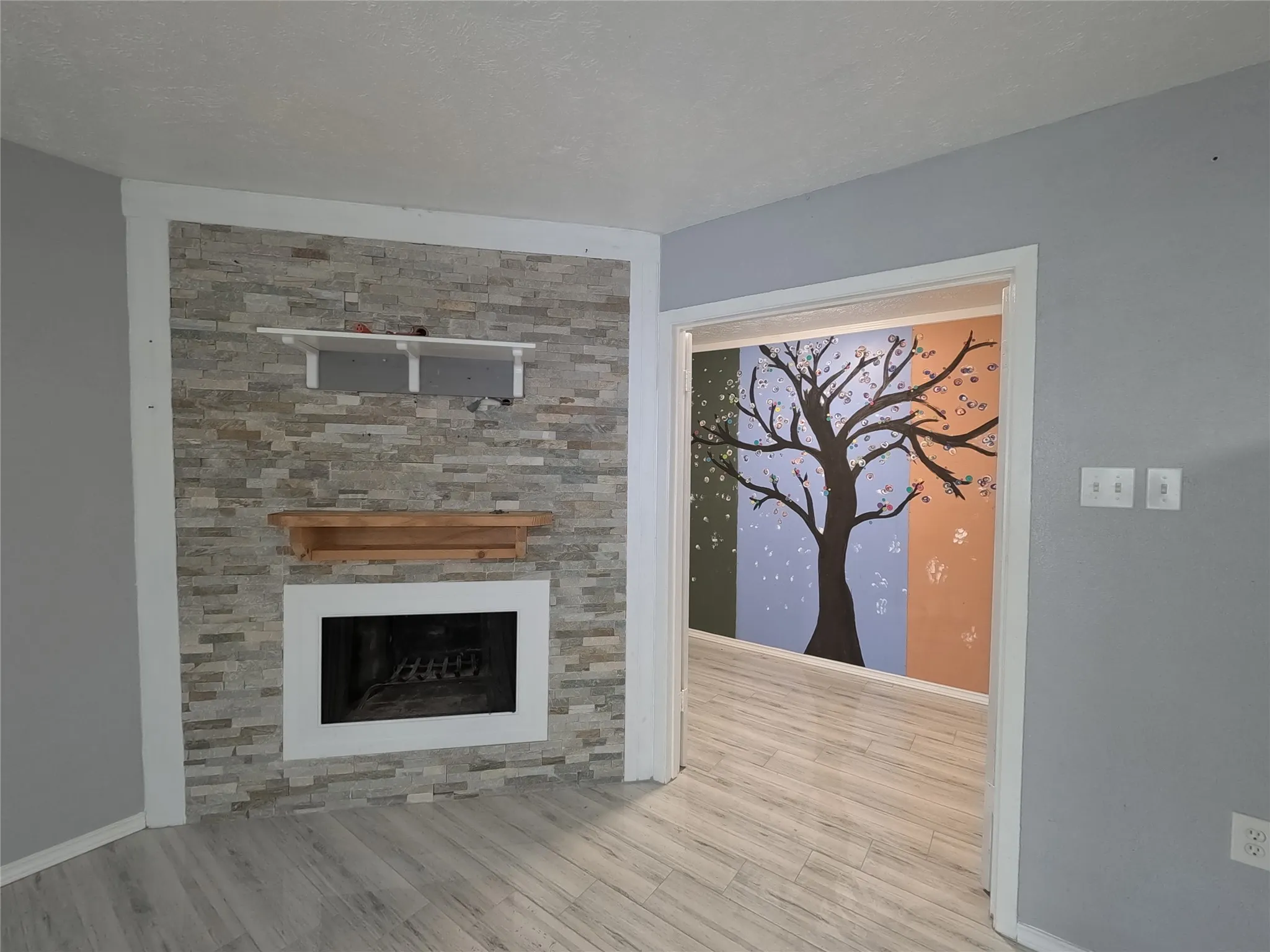 Stacked stone accent wall with fireplace, wood-finish flooring, and a decorative wall mural