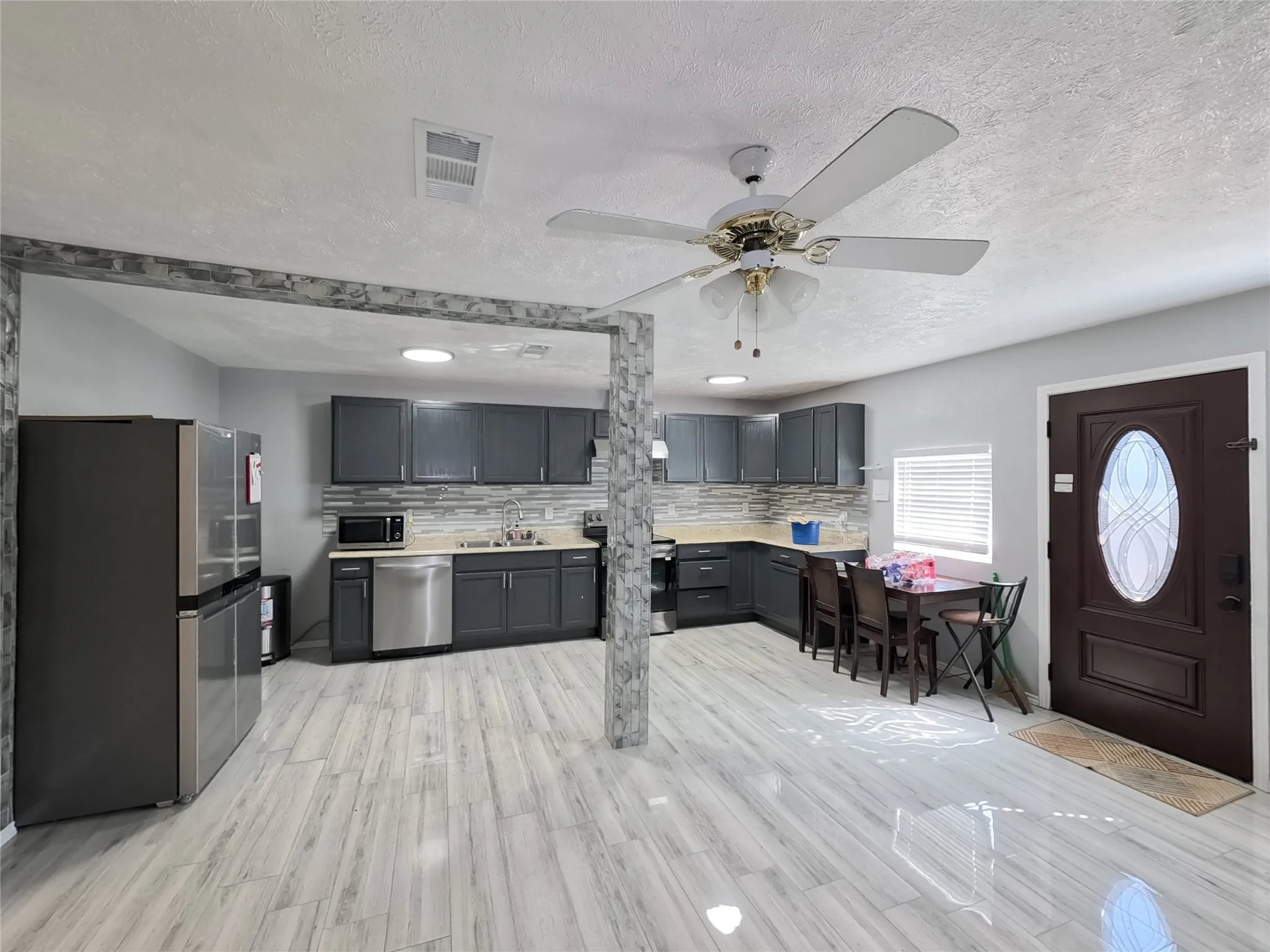 Open-concept kitchen with dark cabinetry, light-toned countertops, and a full tile backsplash