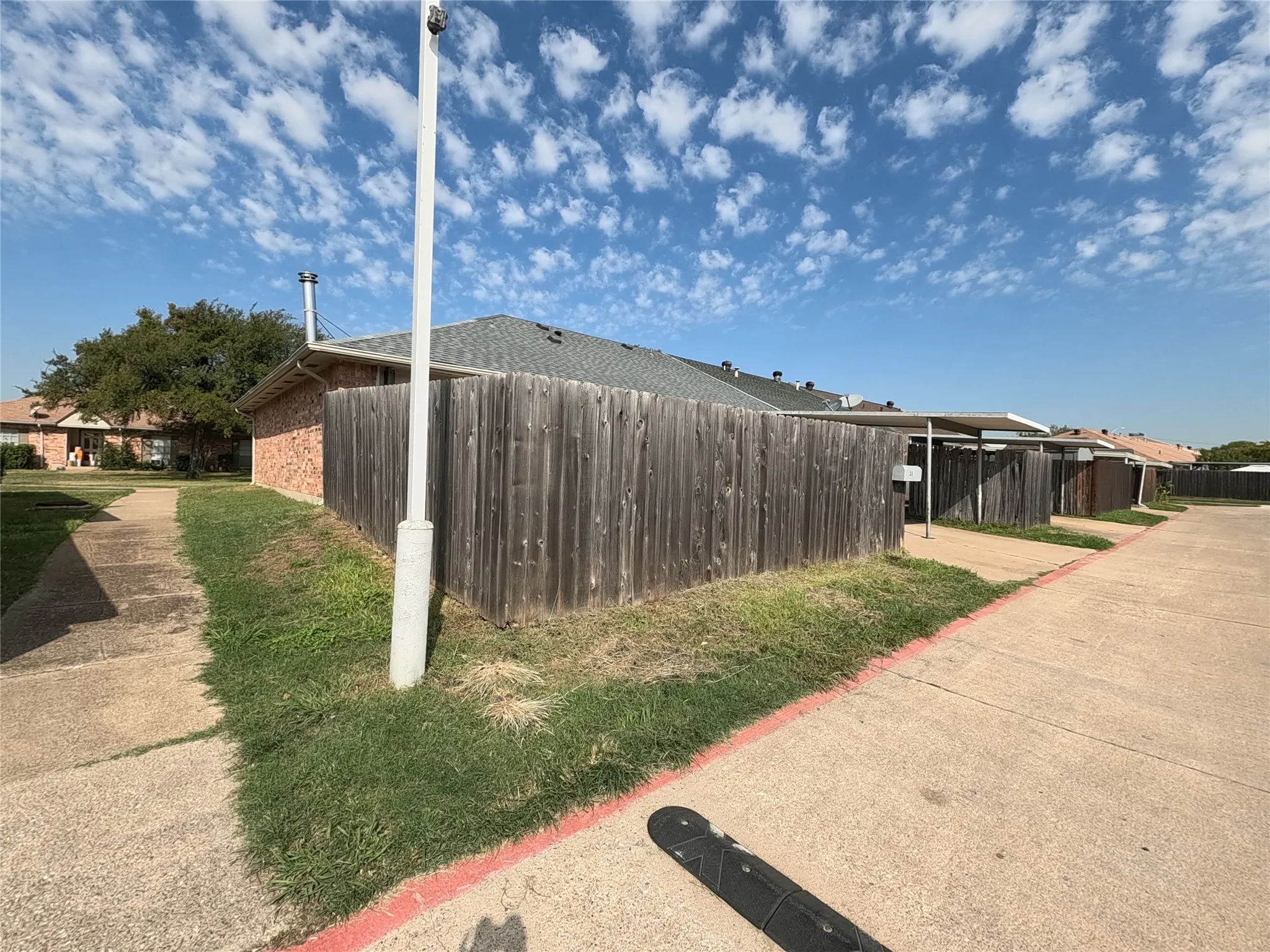 Brick exterior with a gray shingle roof, wood privacy fencing, and multiple covered parking structures