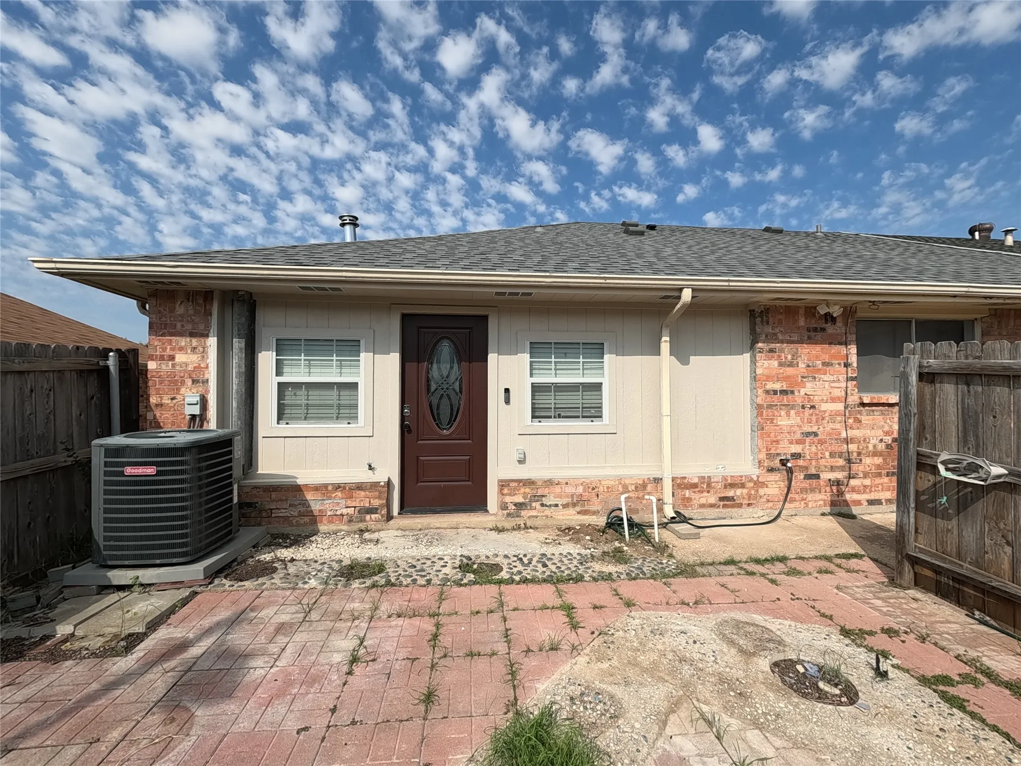 Brick and siding exterior featuring a dark paneled entry door with an oval glass insert, two windows with blinds, and a shingle​​‌​​​​‌​​‌‌​‌‌​​​‌‌​‌​‌​‌​​​‌​​ roof